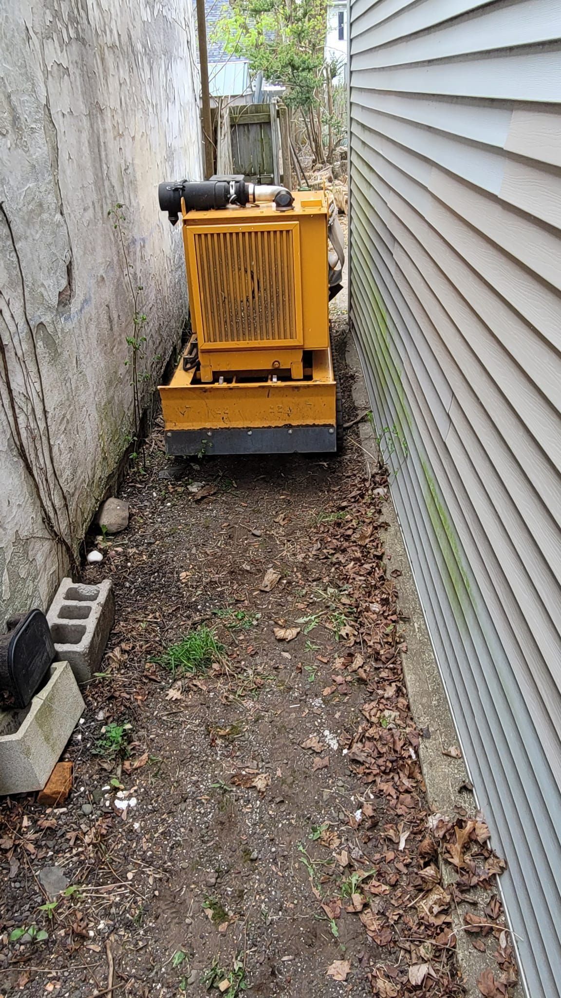 Yellow compact machine in a narrow gravel alley between two buildings.