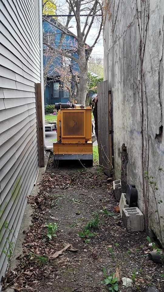 Narrow alley with a yellow dumpster between house siding and a weathered wooden fence.