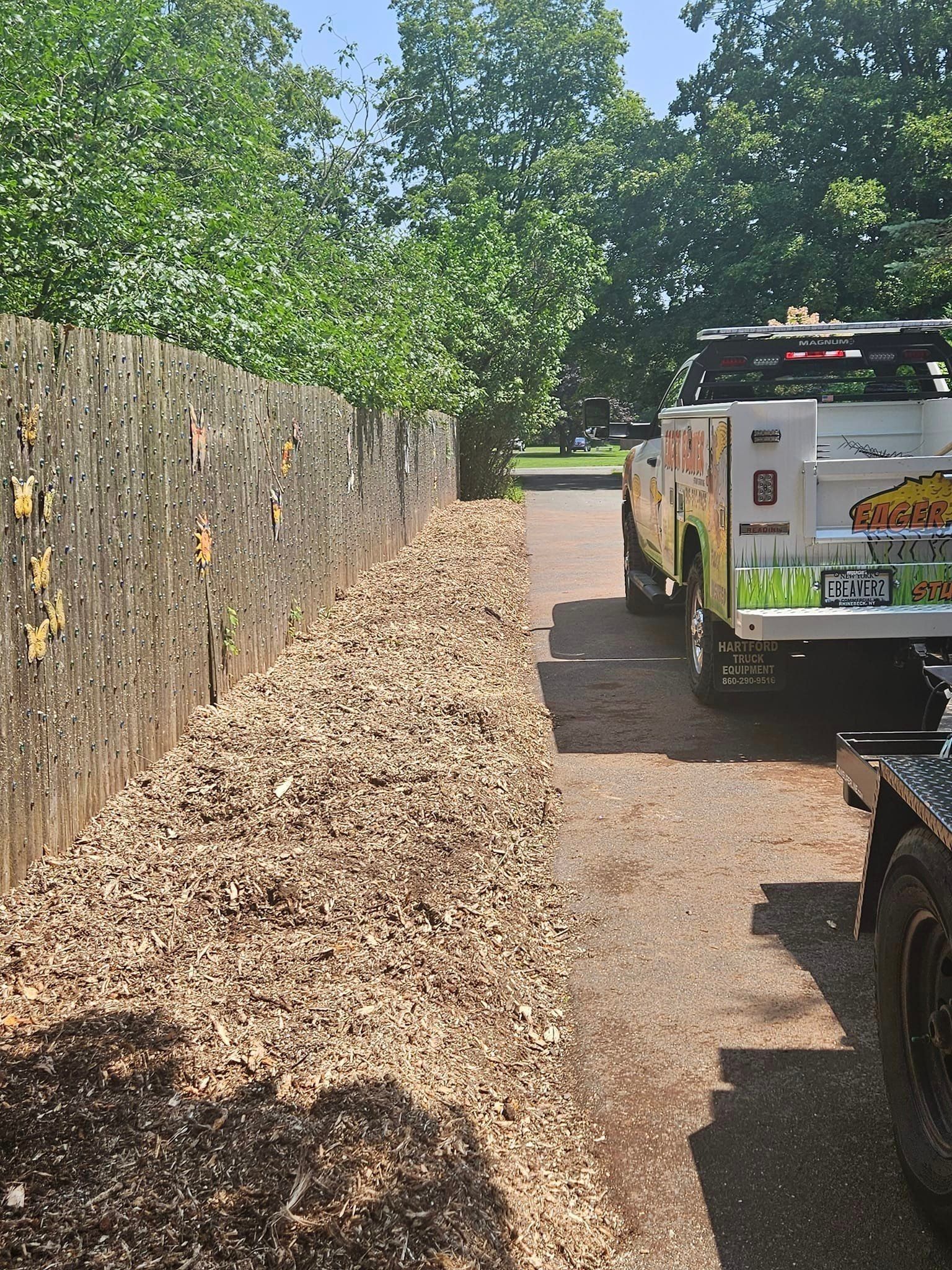 A long pile of leaves along a fence beside a utility truck on a sunny driveway.