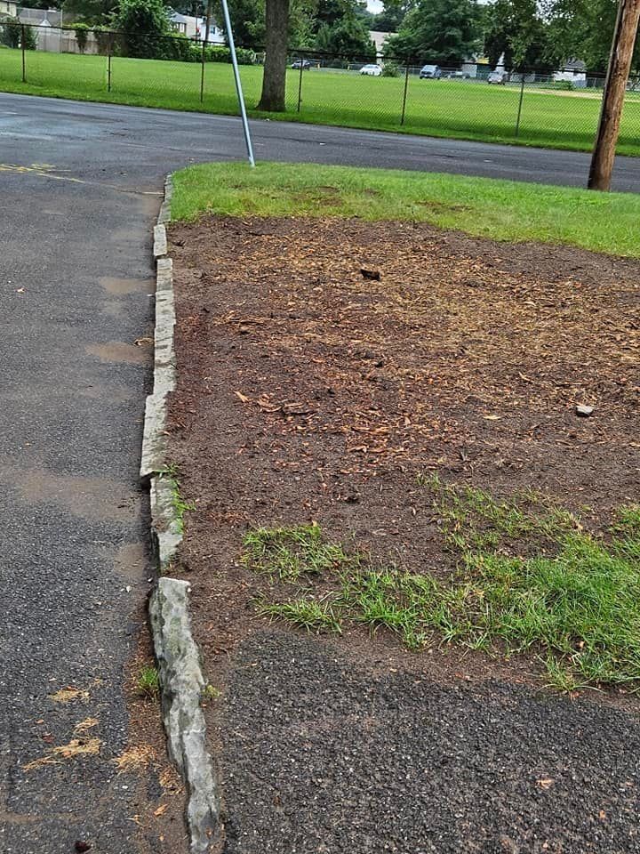 Curb edging a mulch bed beside an asphalt driveway and grassy area in a park-like setting