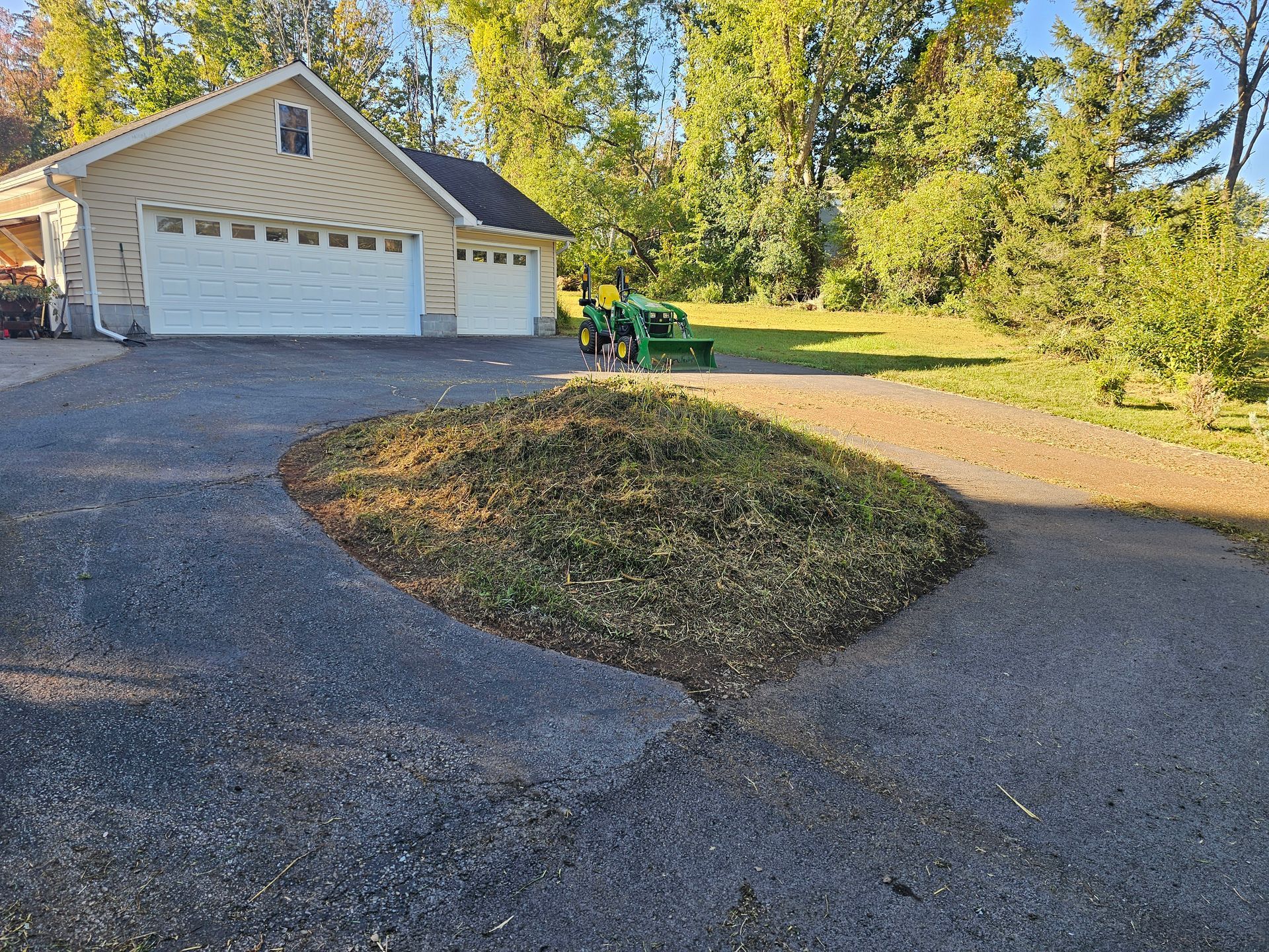 Gravel driveway leading to a white garage beside a grassy yard and trees in warm sunlight