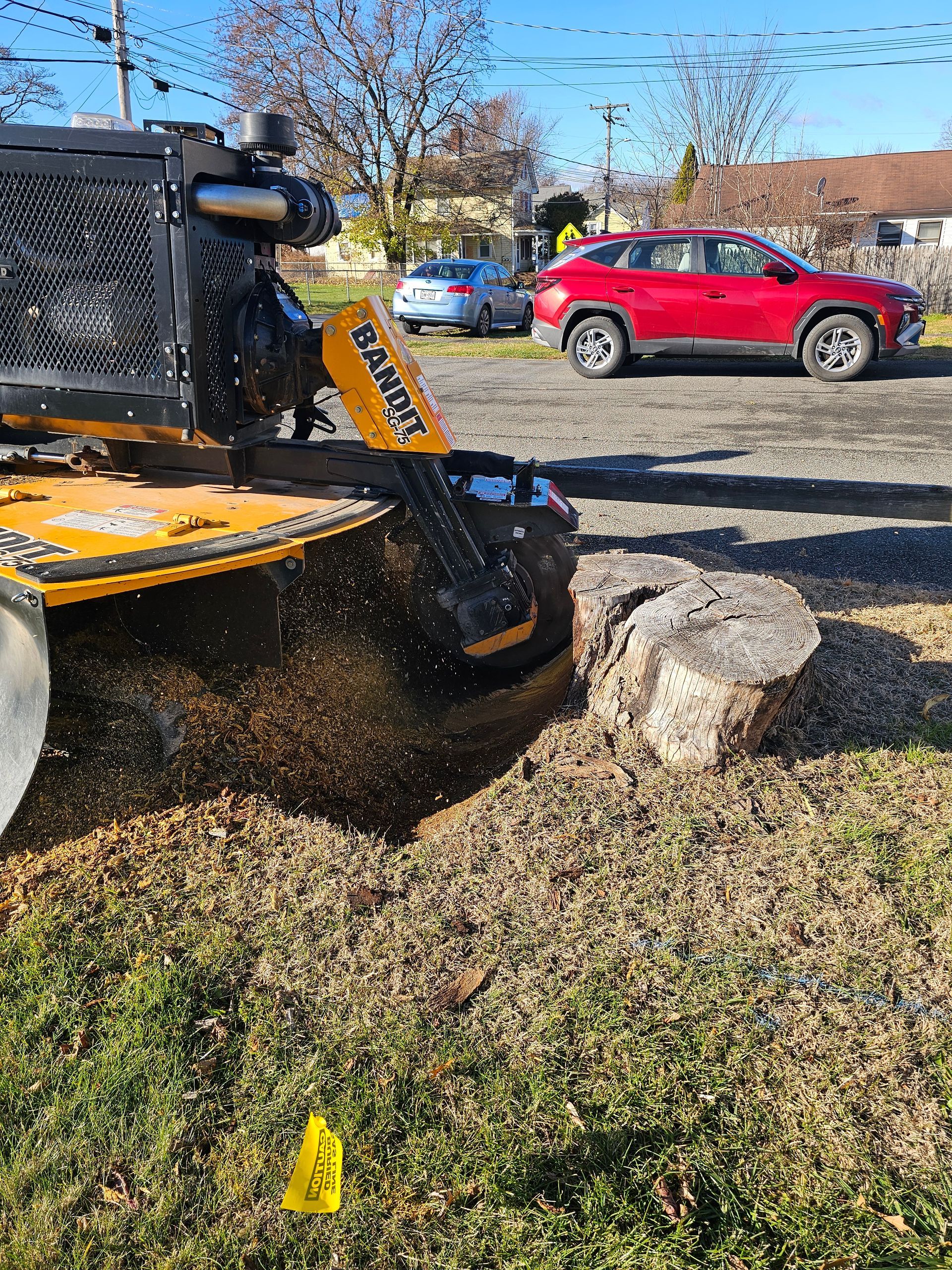 Yellow skid steer pushing rock in a yard beside a red SUV and house, kicking up dirt and debris