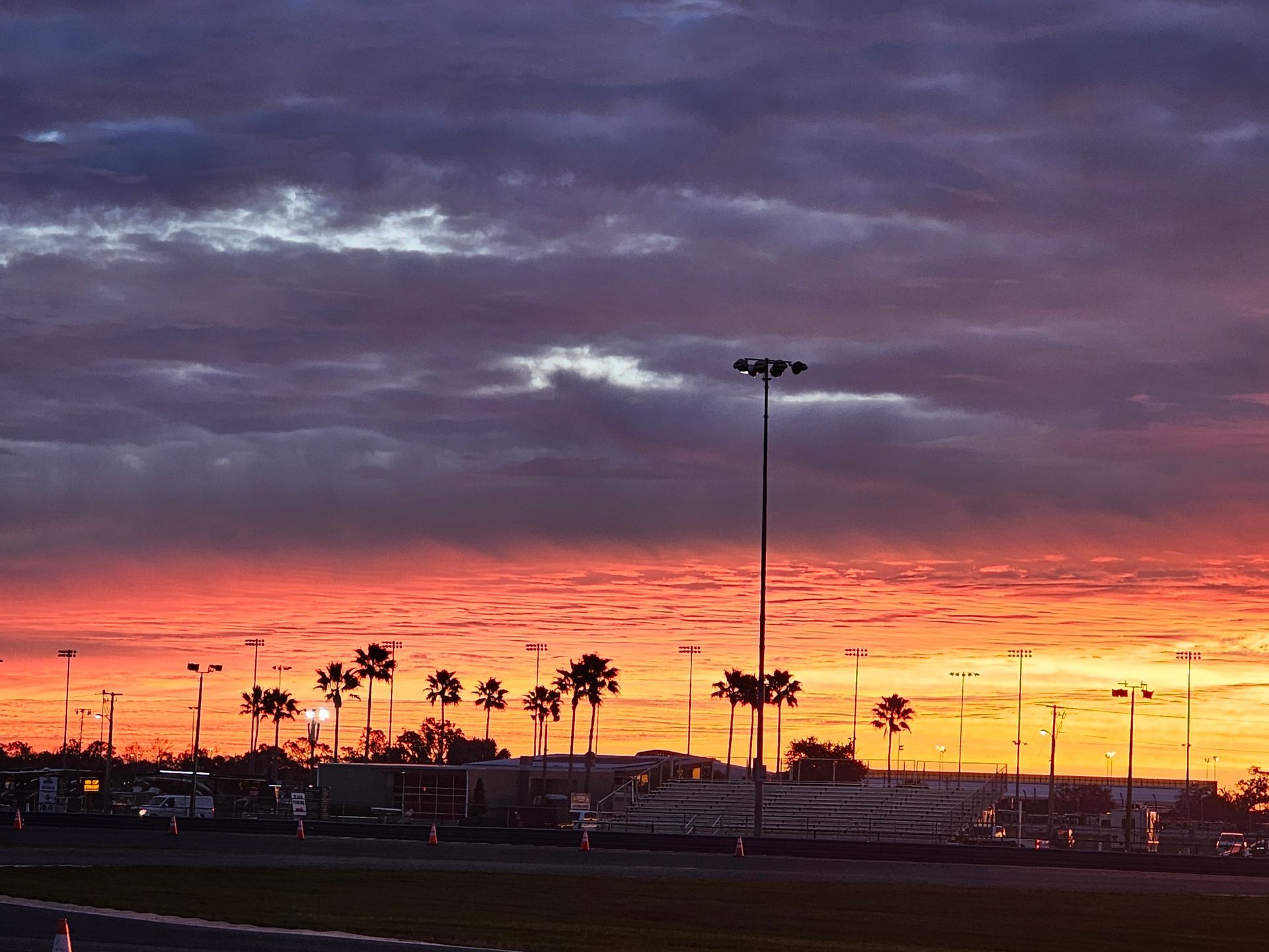 Sunset over a parking lot with silhouetted palm trees and streetlights under a purple-orange sky