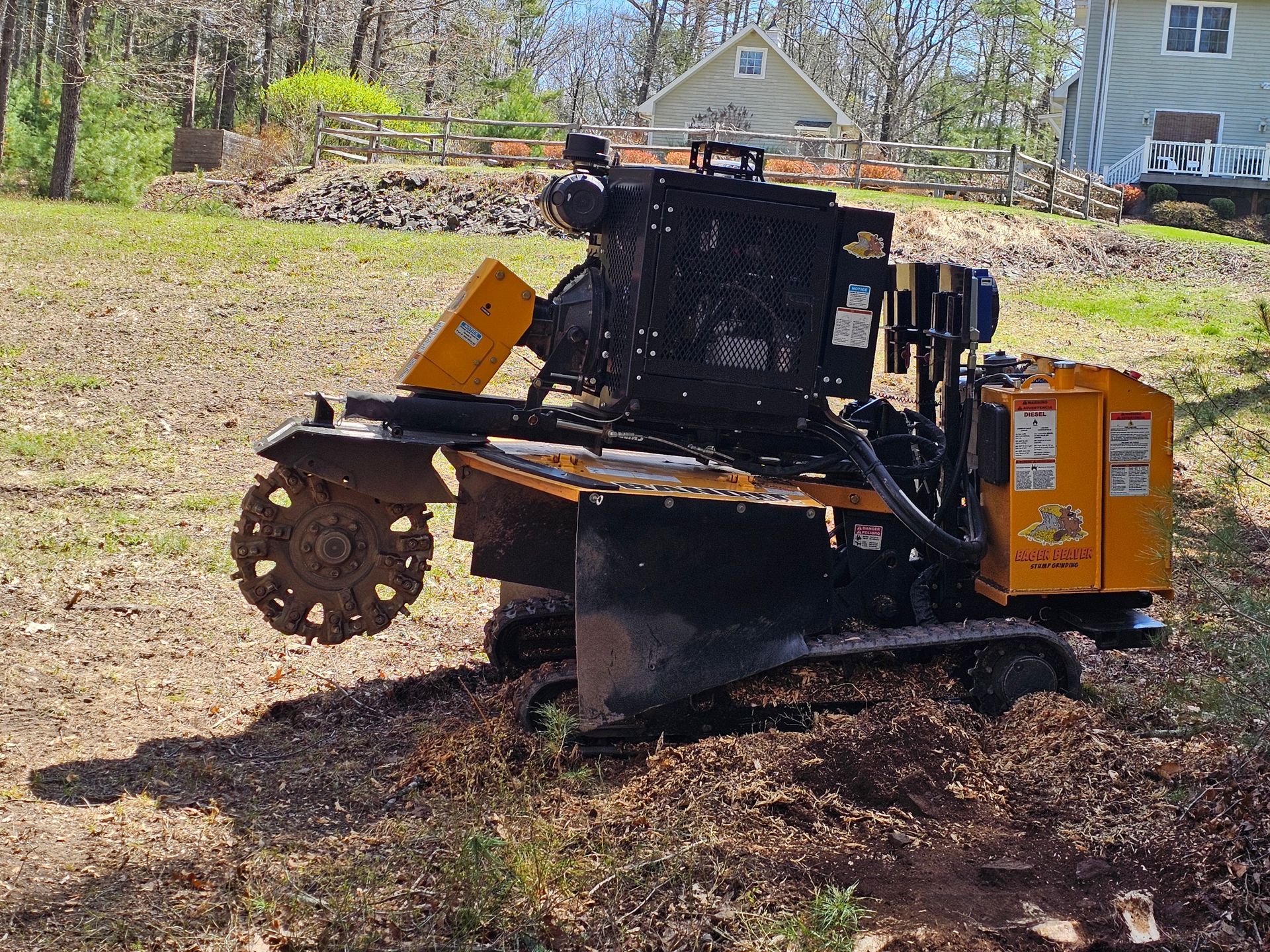 Compact tracked stump grinder with orange engine housing working in a yard near a house