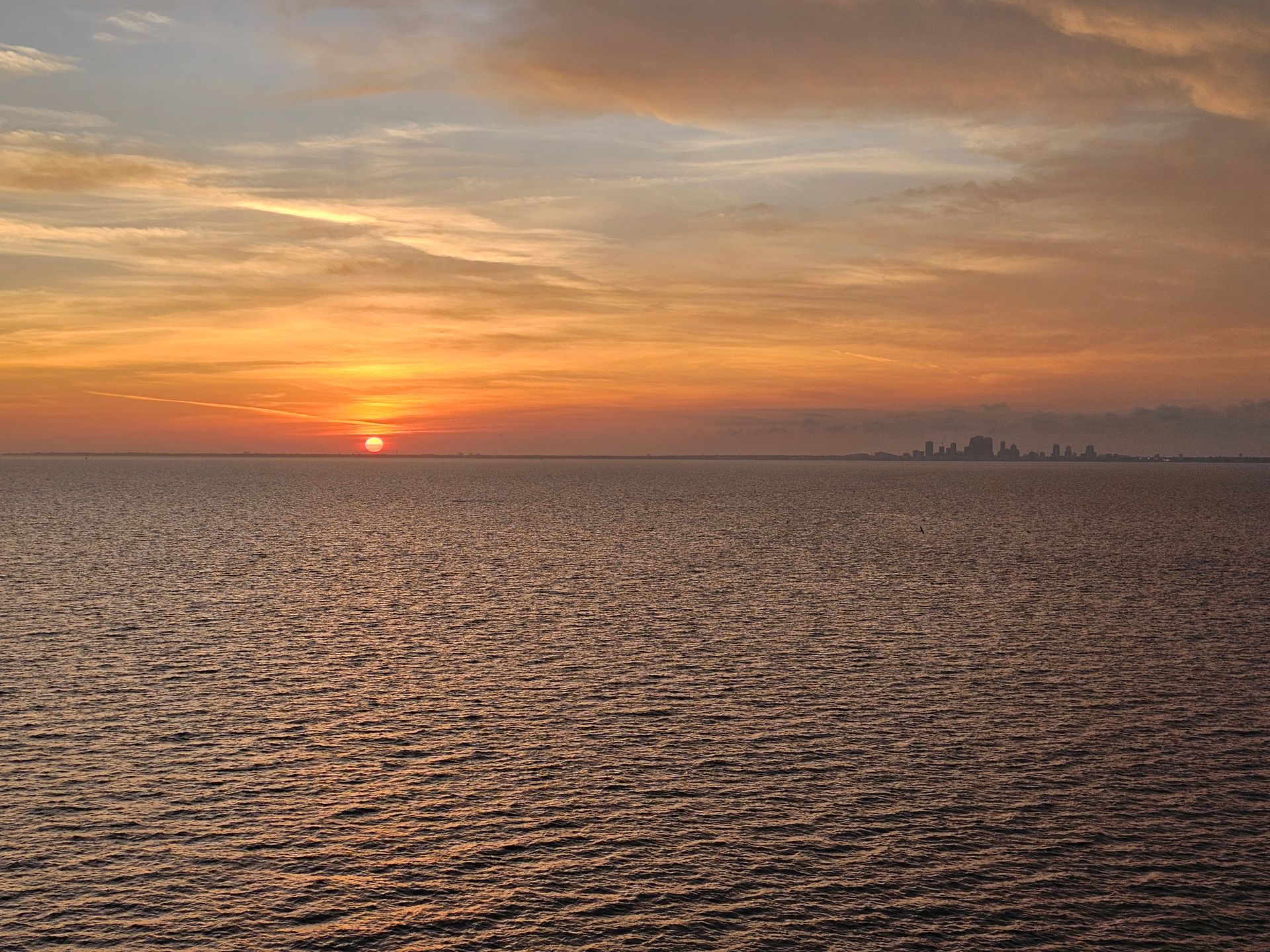 Sunset over a rippling sea with a distant city skyline on the horizon