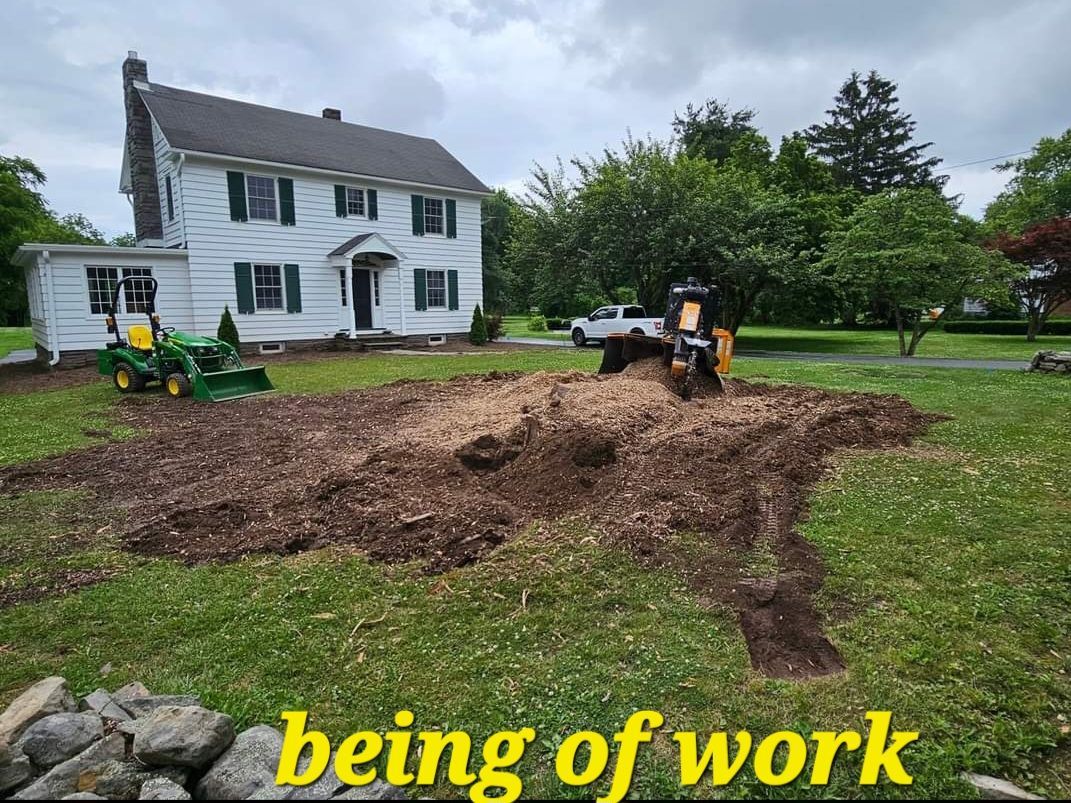 Landscaping work in progress in a muddy yard beside a white house, with a small tractor and piles of dirt.
