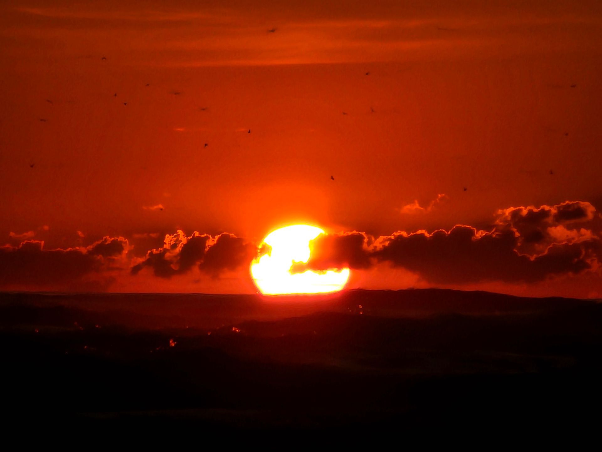 Fiery orange sunset over a dark horizon with scattered clouds