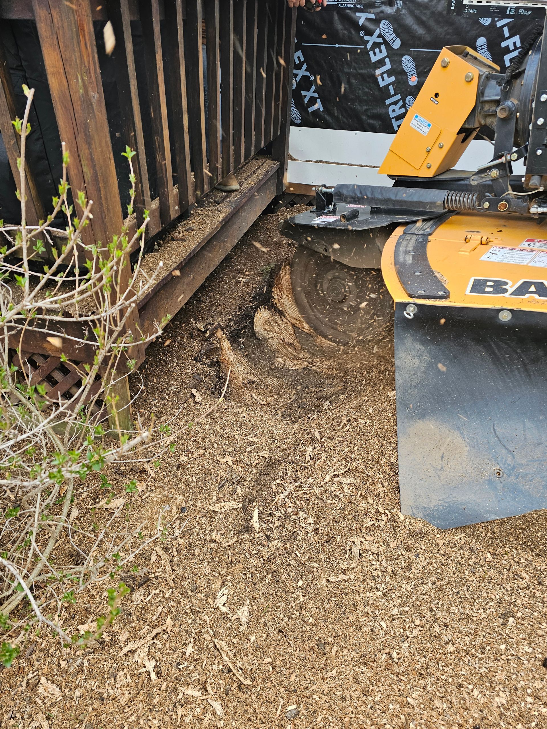 Yellow construction machine beside a rusted fence, pushing dirt and gravel along a narrow path.
