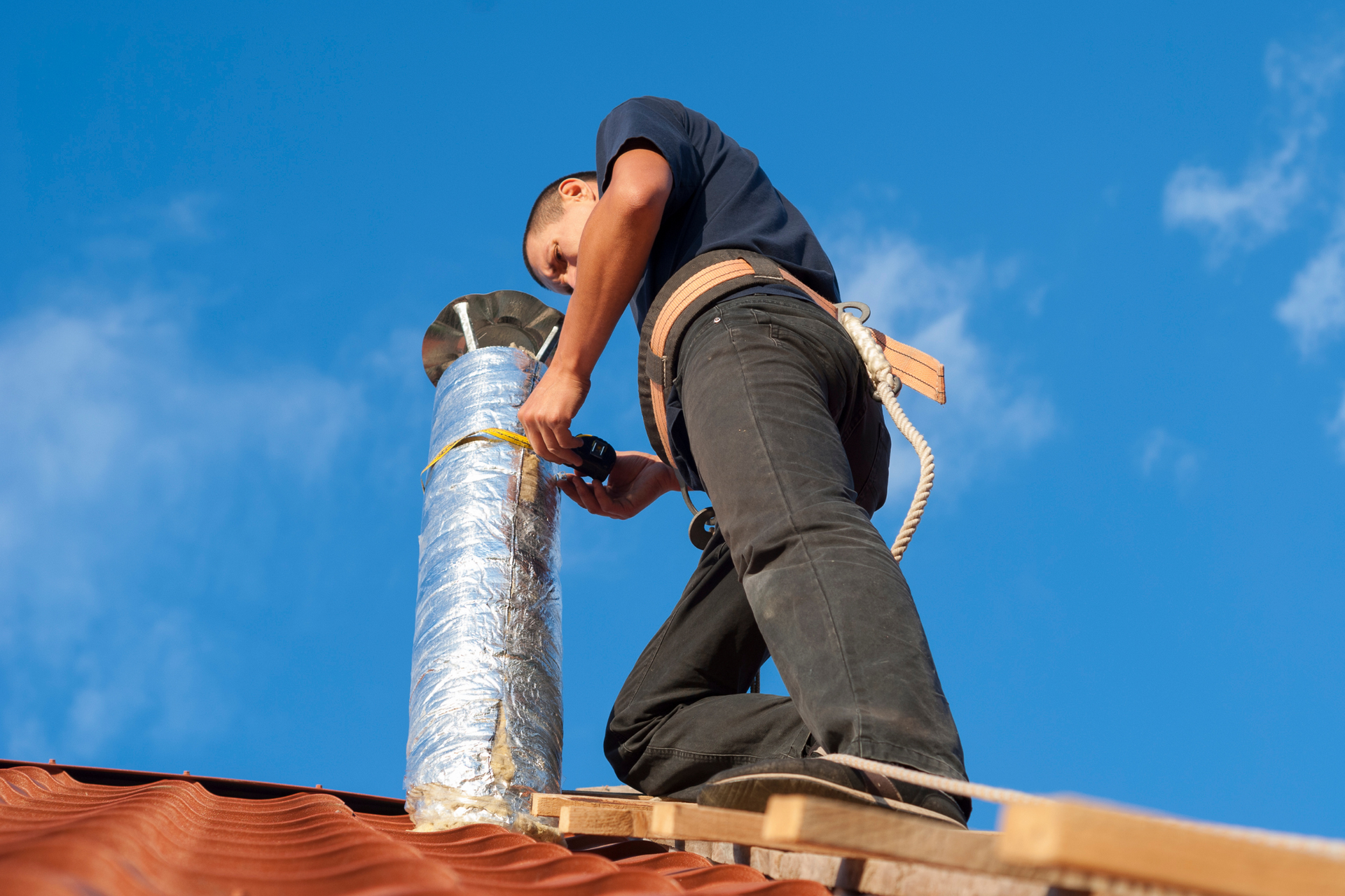 A man is working on an HVAC chimney on top of a roof.