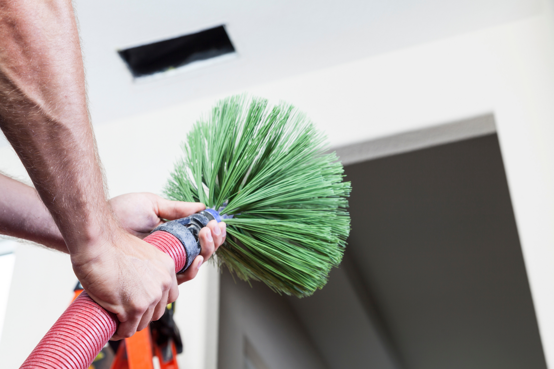 A man is holding a hose used to clean air ducts, with a green brush attached to it.