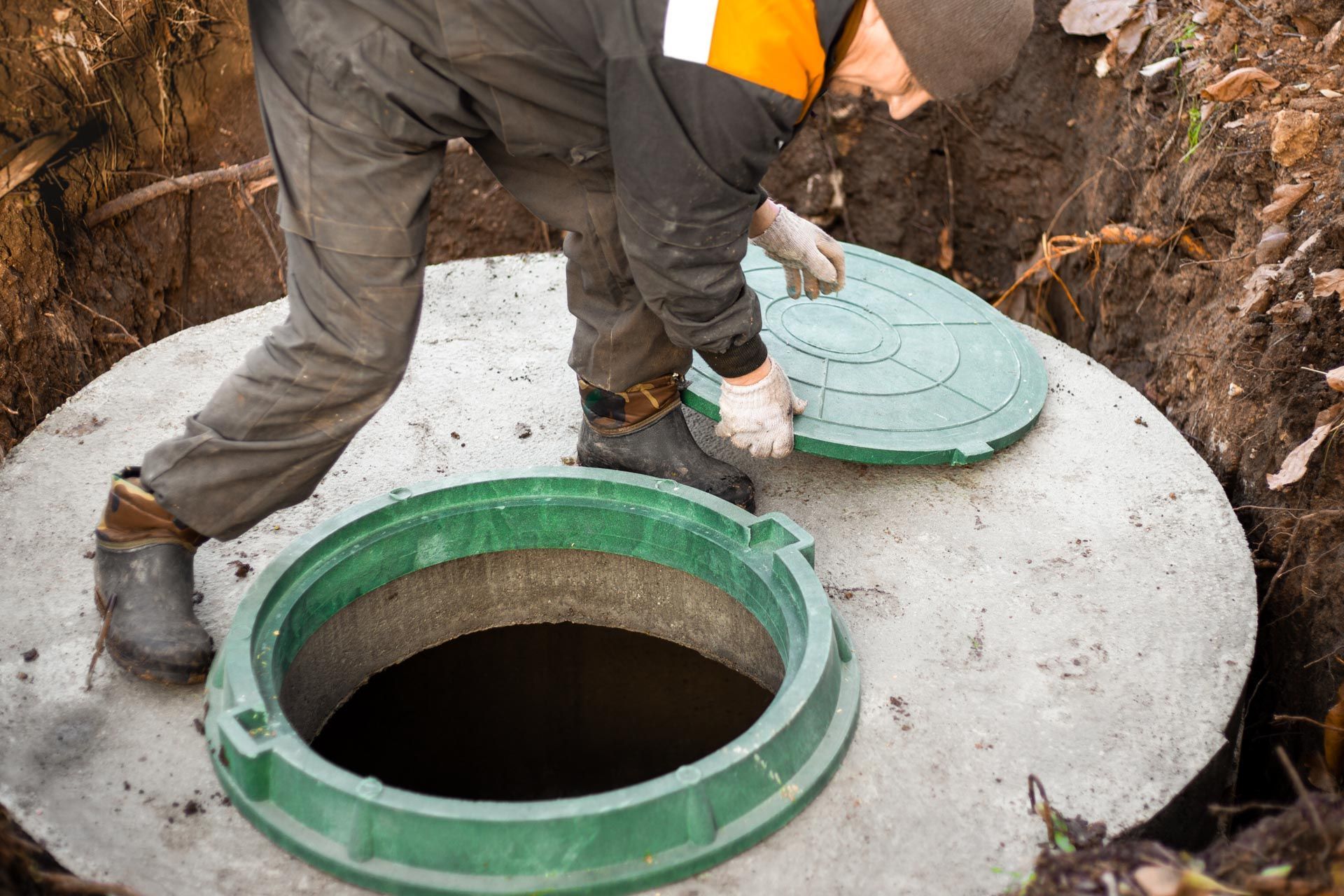 Worker opening a green manhole cover over a concrete septic chamber outdoors