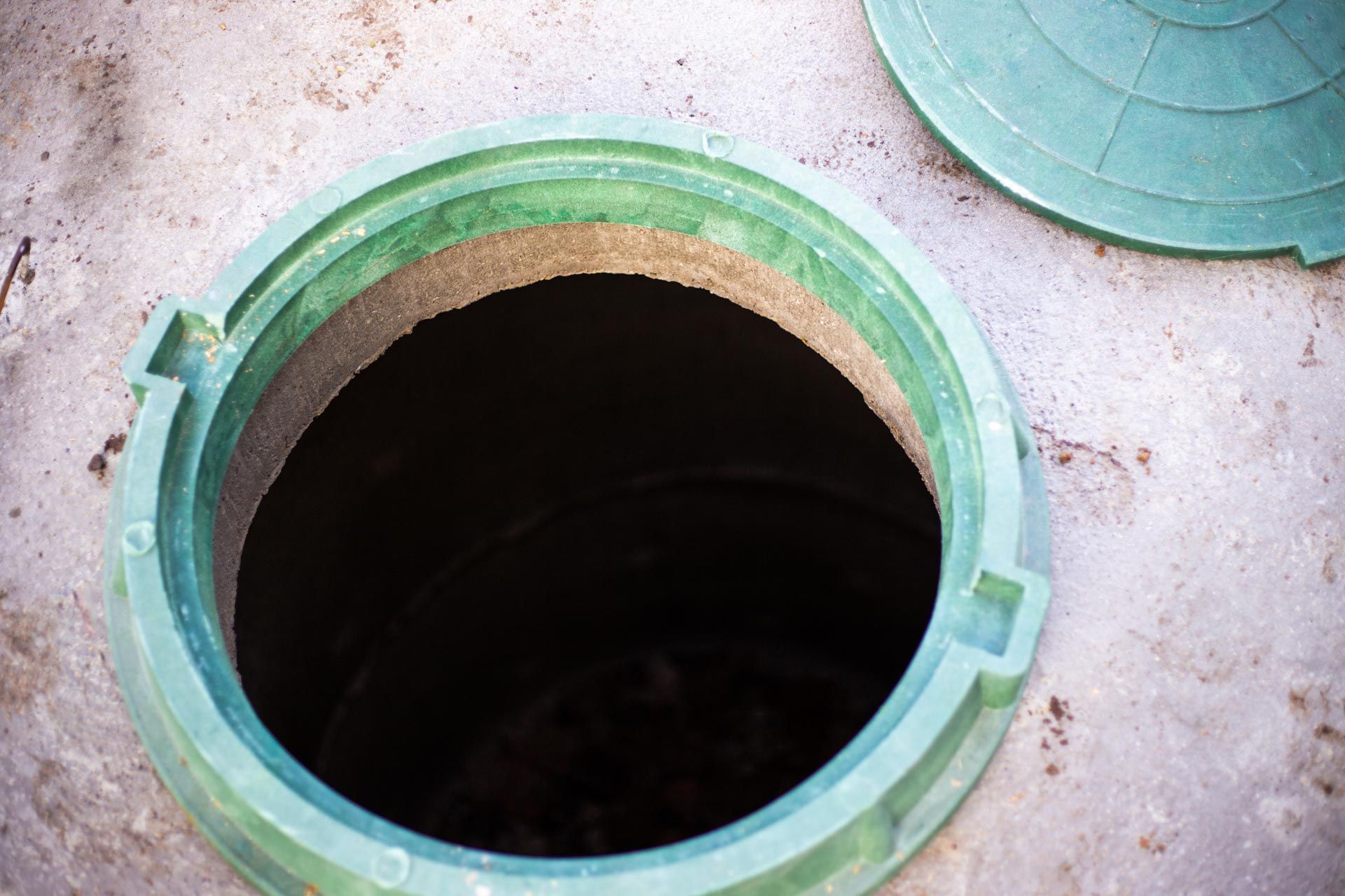Open manhole with red hose extending into it on a concrete surface