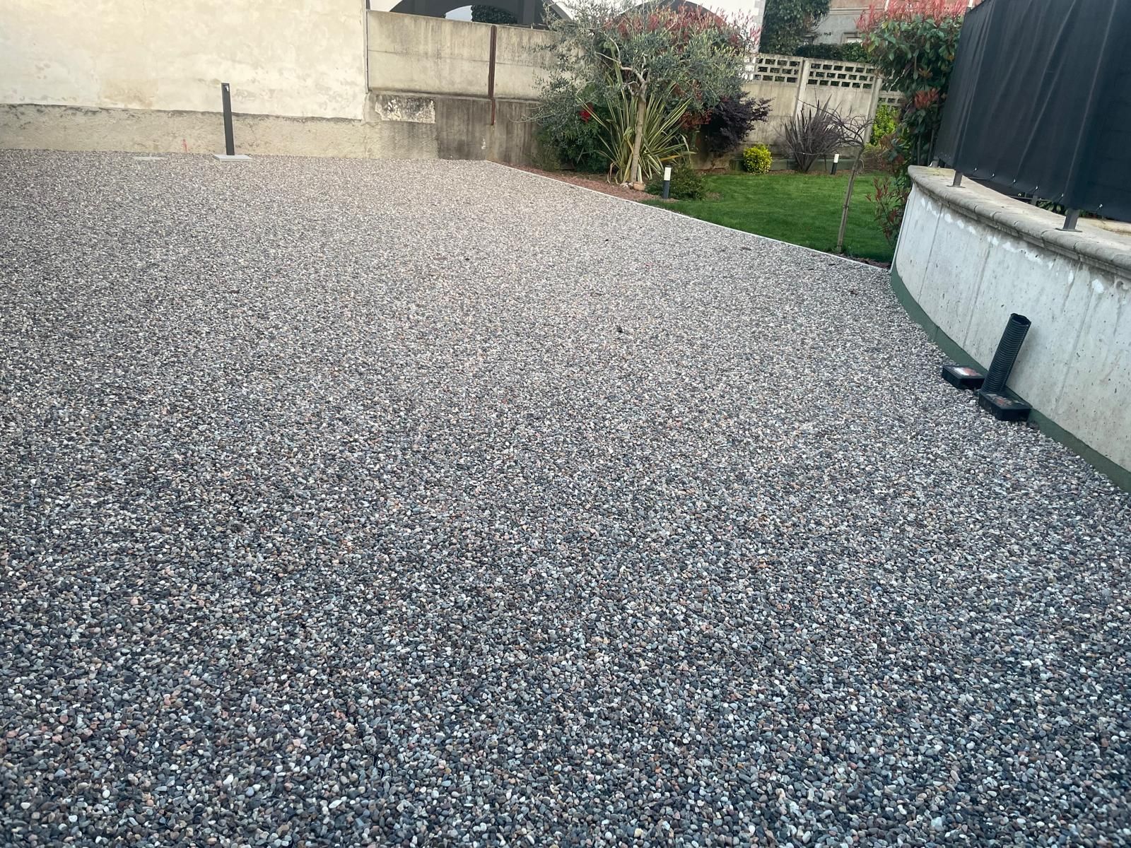 Patio posteriore ricoperto di ghiaia accanto a una casa, con un piccolo giardino e una recinzione sullo sfondo.
