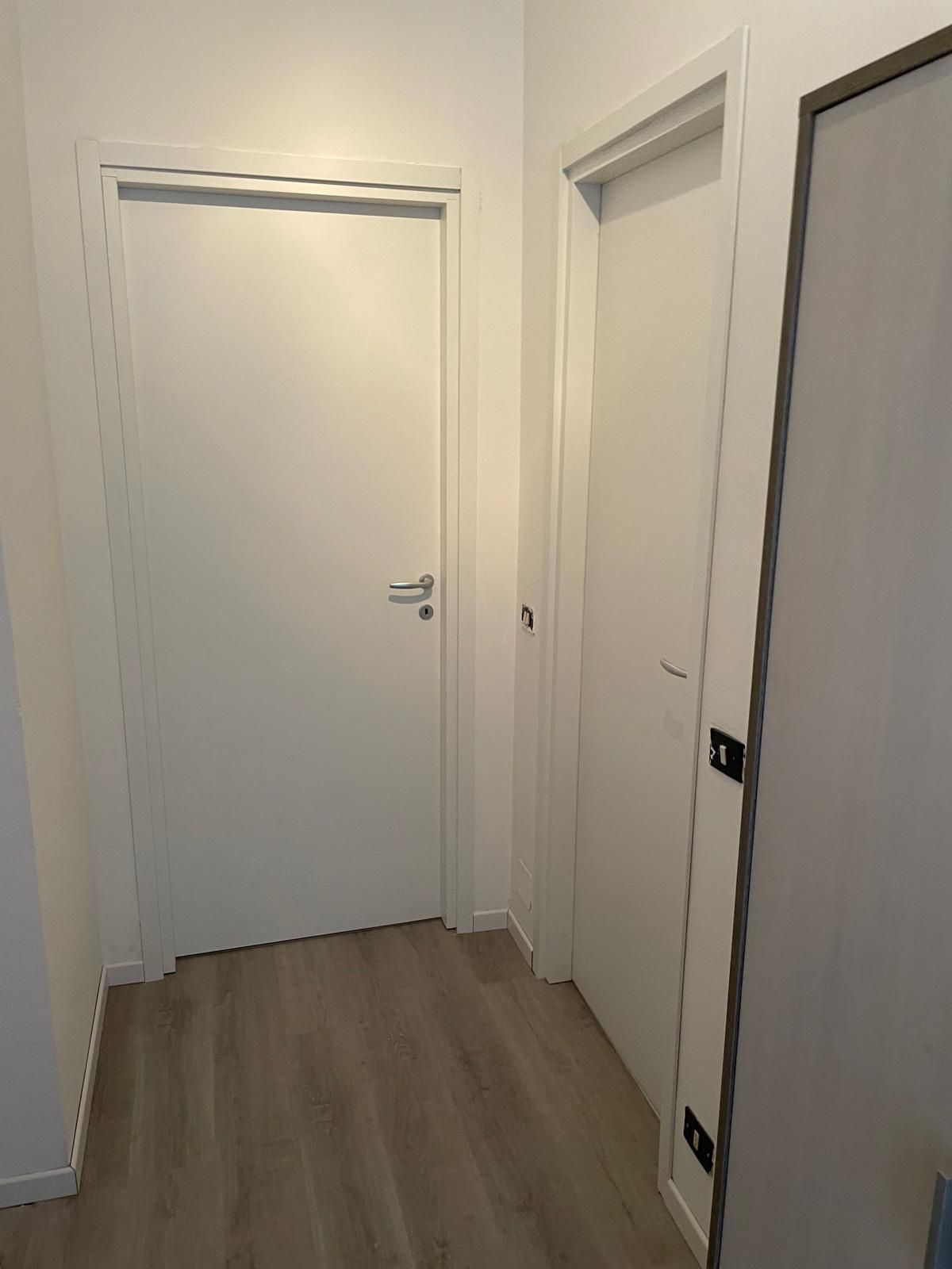 Corridoio vuoto con porte bianche e pavimento in legno chiaro.