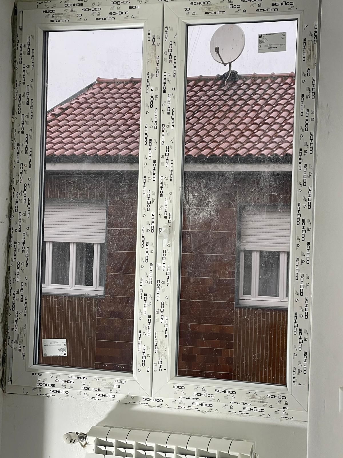 Telaio di finestra bianco scrostato che si affaccia su tetti di tegole rosse e case di mattoni vicine