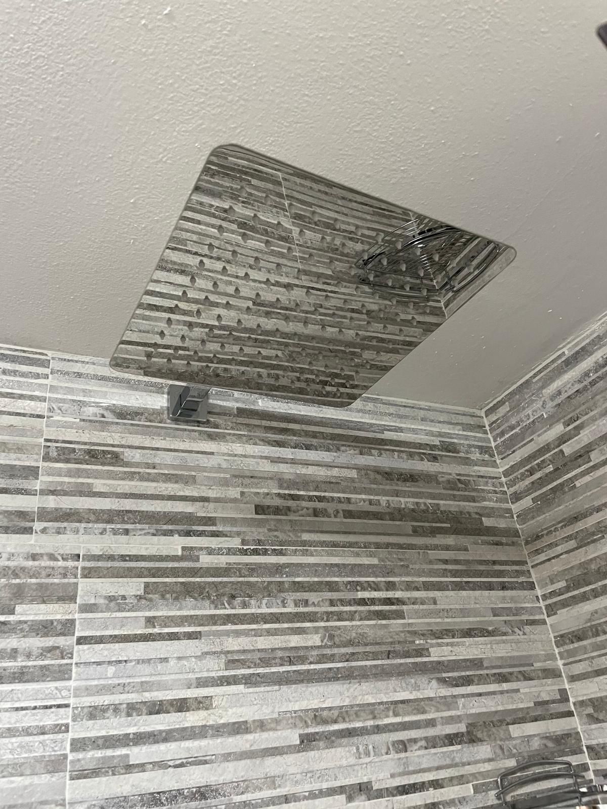 Soffitto della doccia del bagno con una macchia rettangolare scura vicino alla ventola e pareti piastrellate.