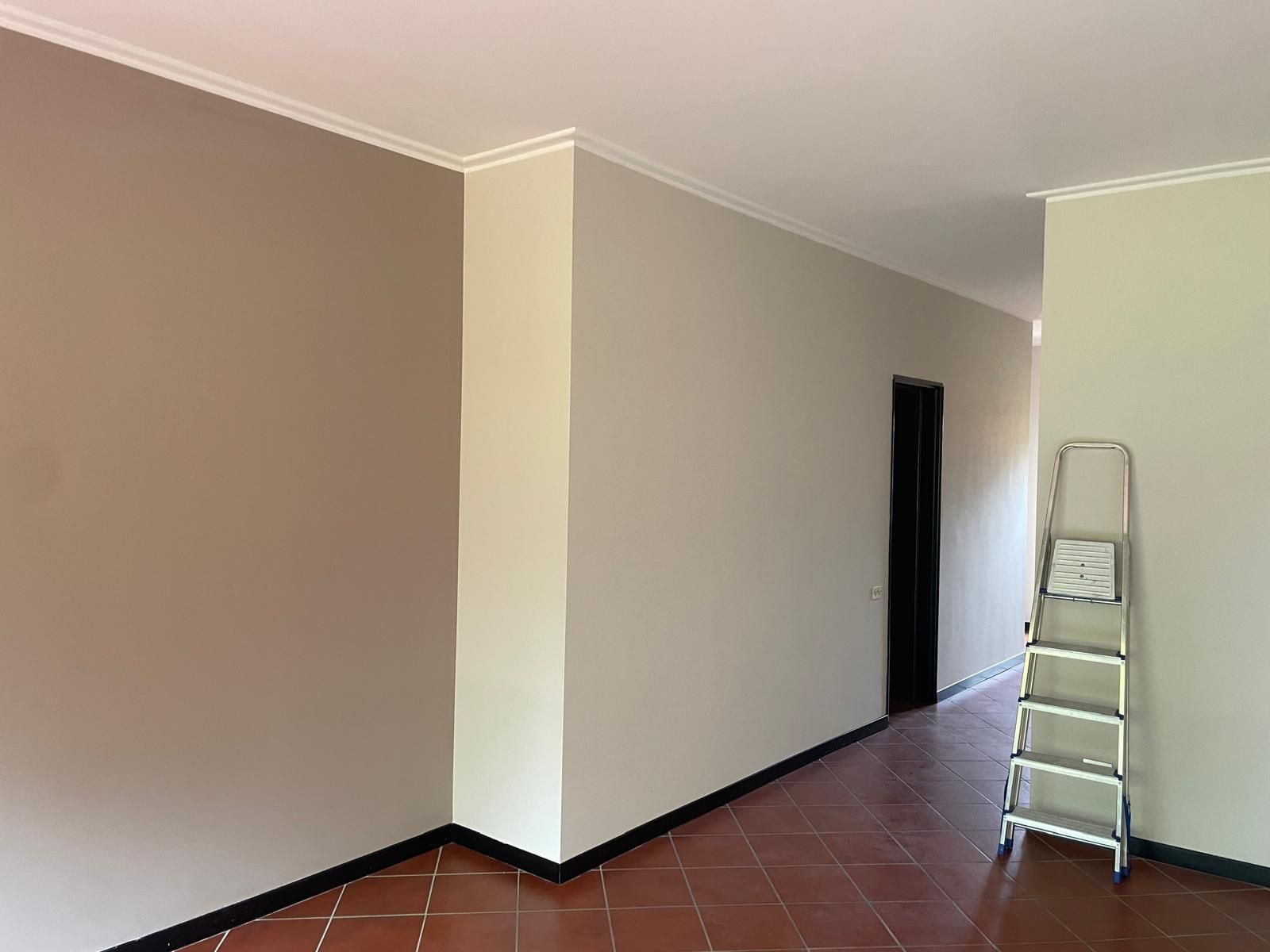Corridoio vuoto con pareti beige, finiture scure, pavimento piastrellato e una scaletta in fondo.