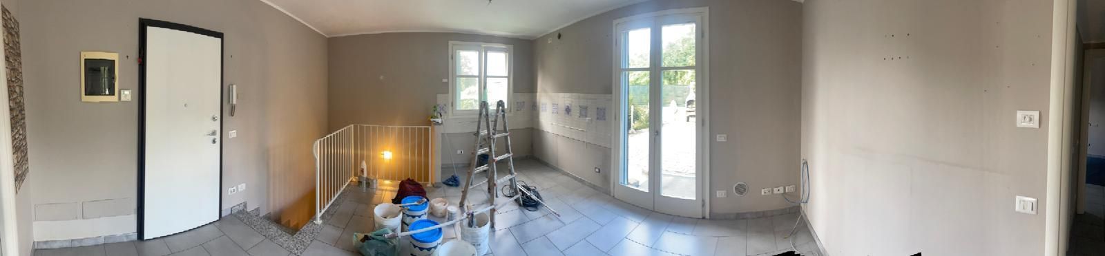 Stanza vuota in fase di ristrutturazione con pareti beige, attrezzi sparsi, una scala e finestre luminose.