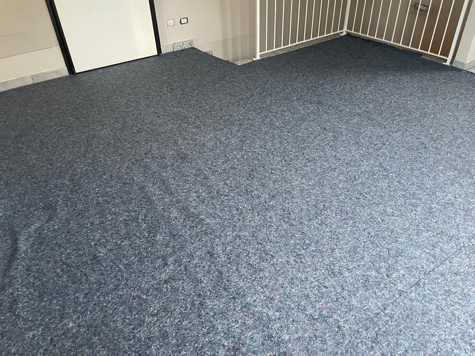 Stanza vuota con moquette, pavimento grigio-blu e pareti beige, vicino a una ringhiera.
