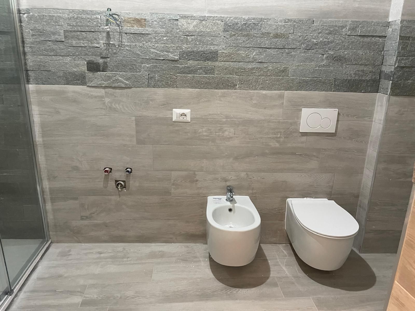Bagno moderno con pareti rivestite in piastrelle di pietra, WC sospeso e piccolo lavabo sospeso.