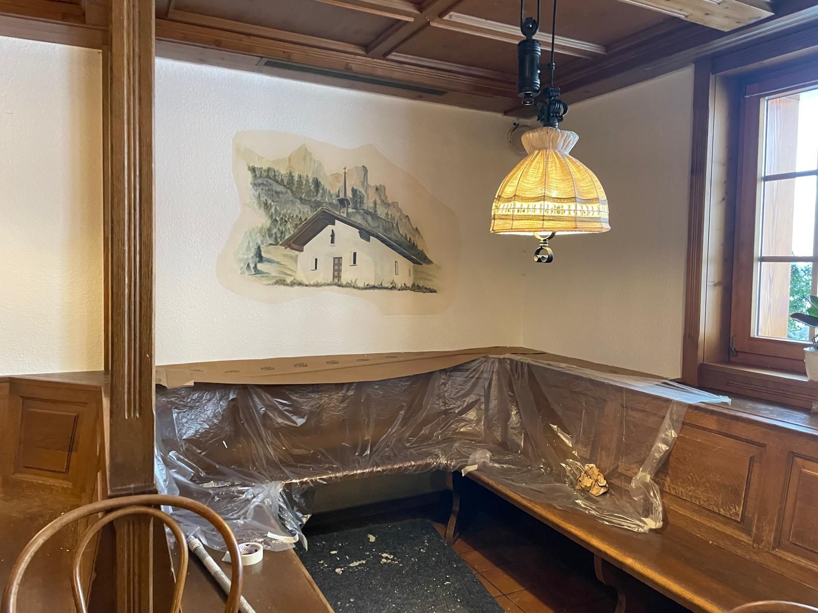 Accogliente divanetto in un angolo di ristorante rivestito in legno, con lampada a sospensione e murale sulla parete.