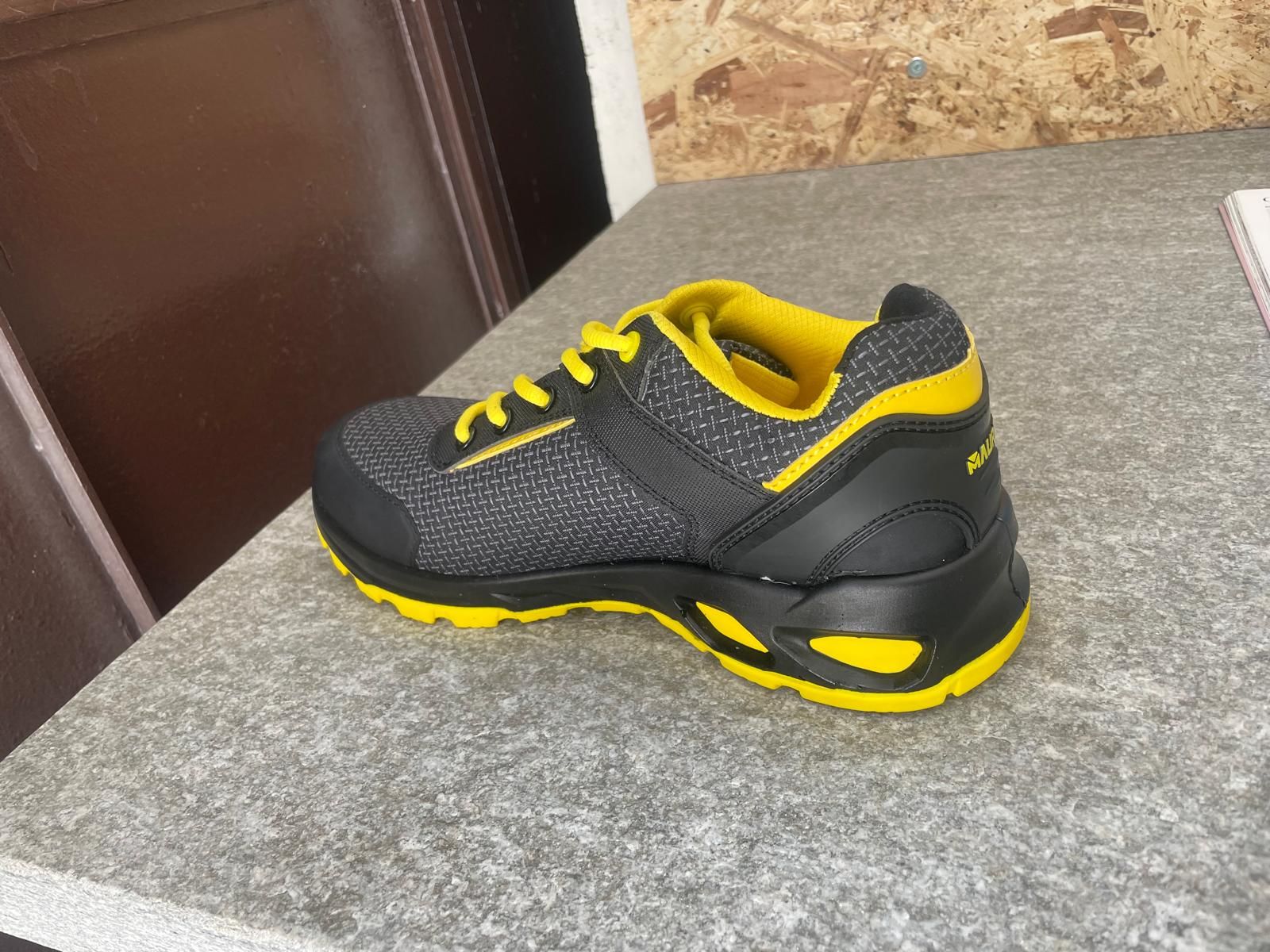 Scarpa sportiva nera e gialla su una superficie grigia, vista laterale
