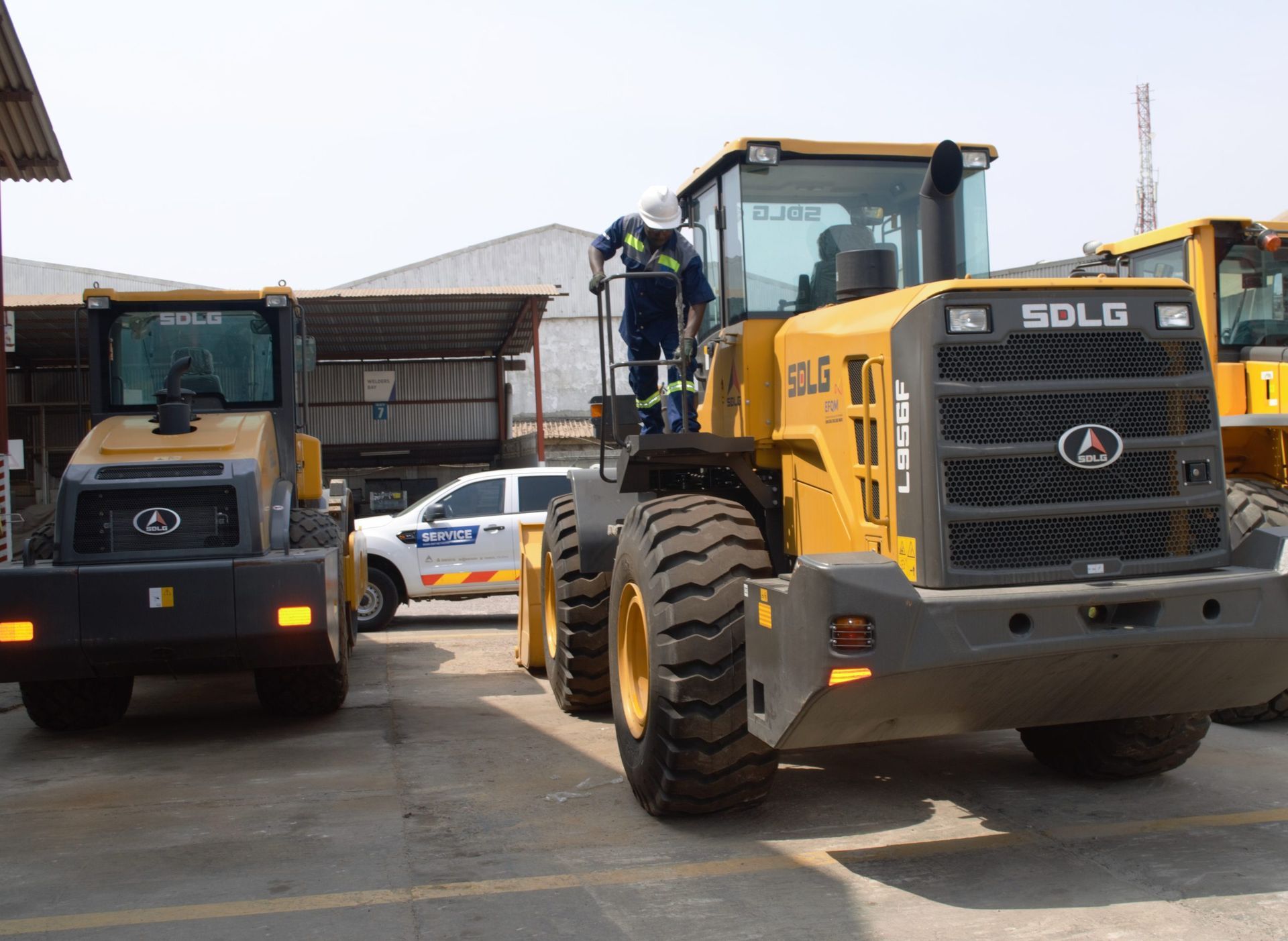 Two yellow SDLG loaders parked in a work yard, one with a person standing on it