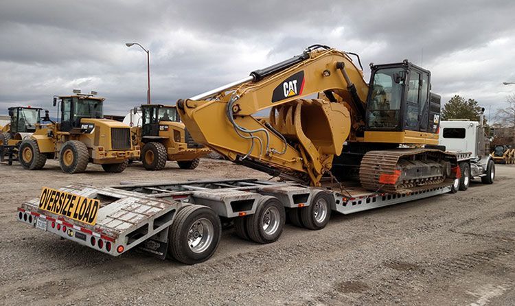 Yellow CAT excavator loaded on a lowboy trailer in an industrial lot