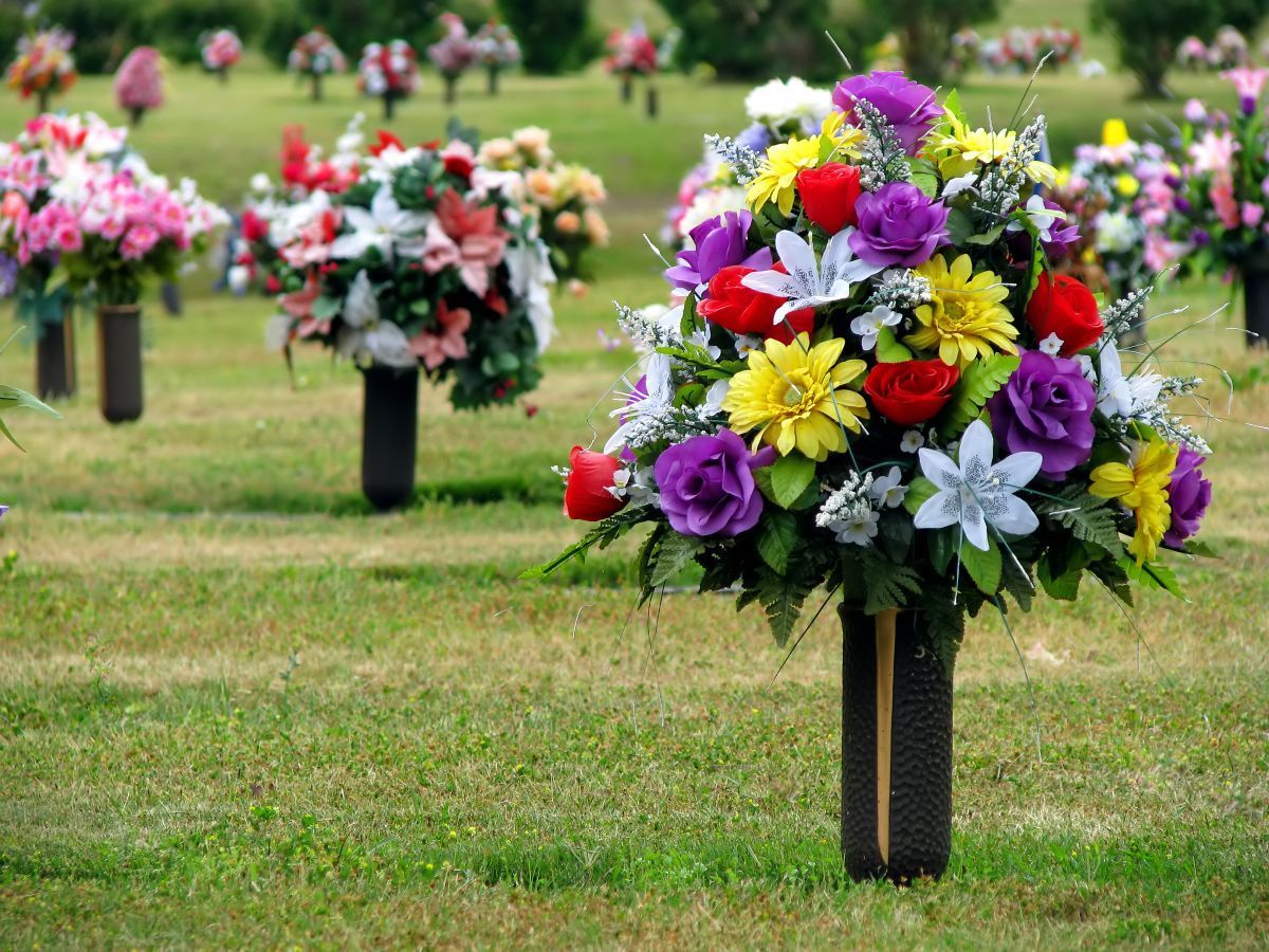 Colorful flower arrangements in vases on green grass at a cemetery.
