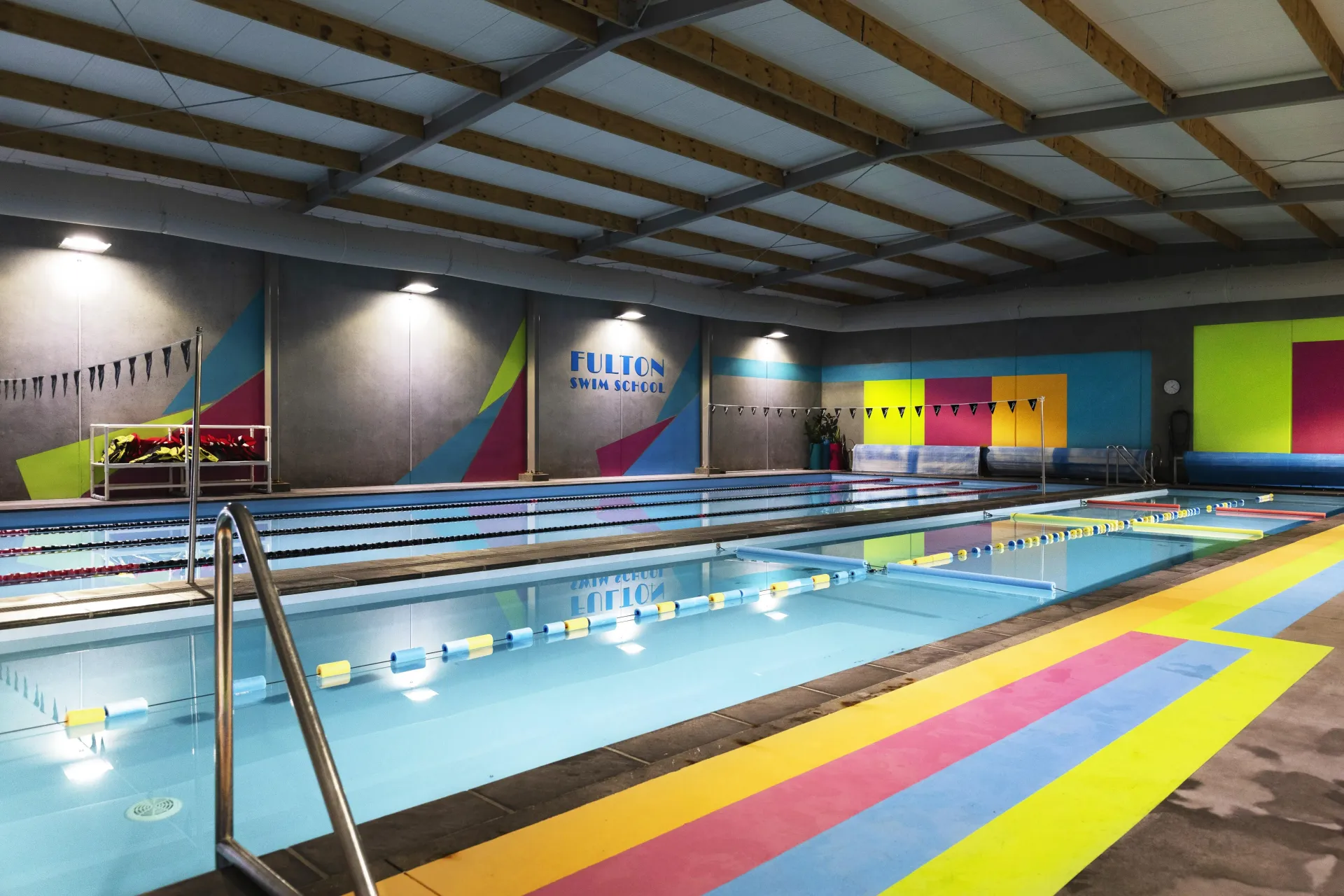 A large indoor swimming pool with a rainbow colored floor.