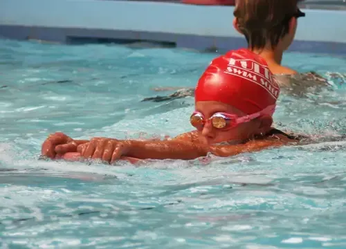 A person wearing a red swim cap and goggles is swimming in a pool.