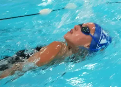 A woman is swimming in a pool wearing a blue swim cap and goggles.
