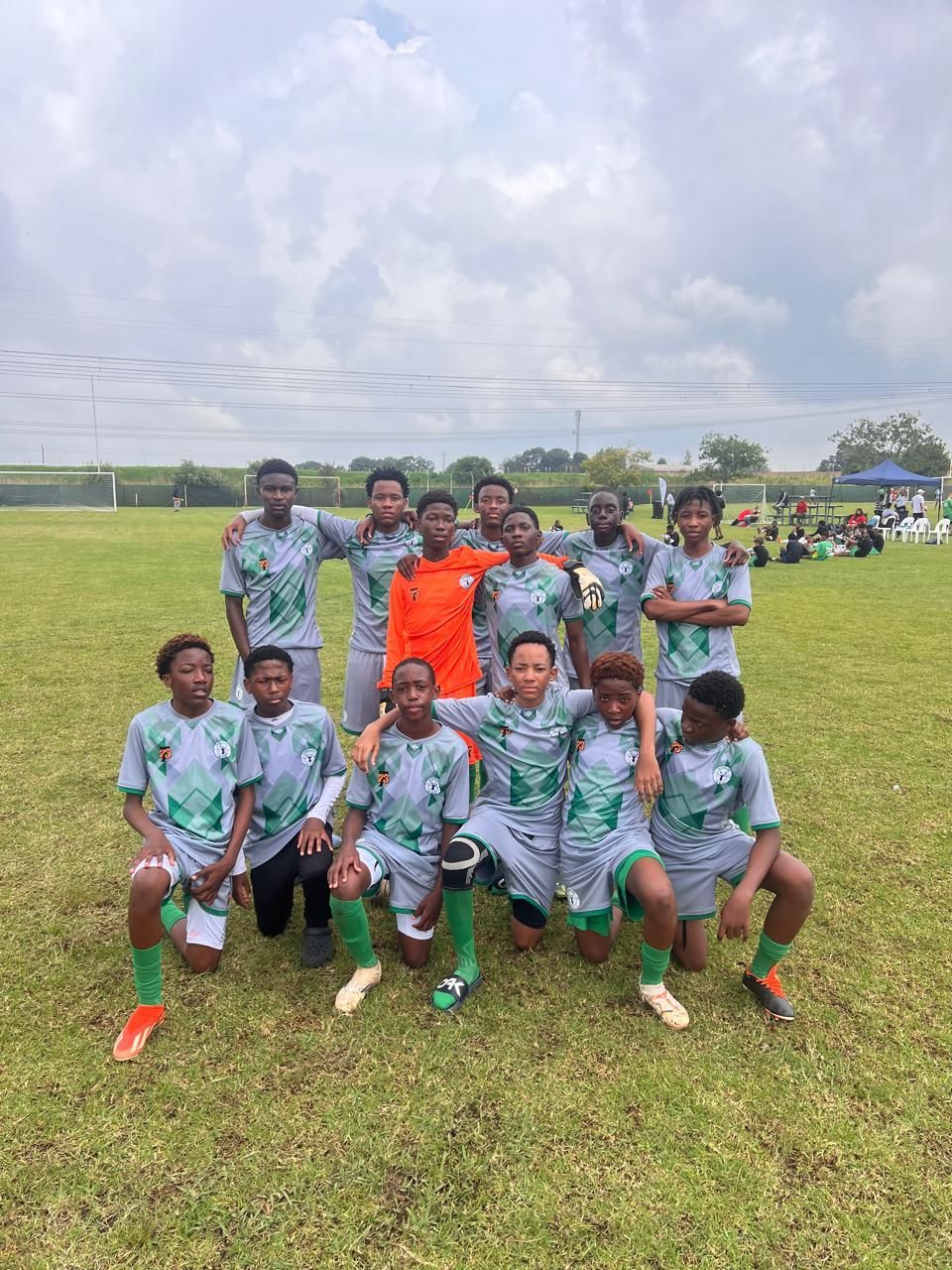A soccer team posing for a photo on a grassy field, wearing matching gray and green jerseys.