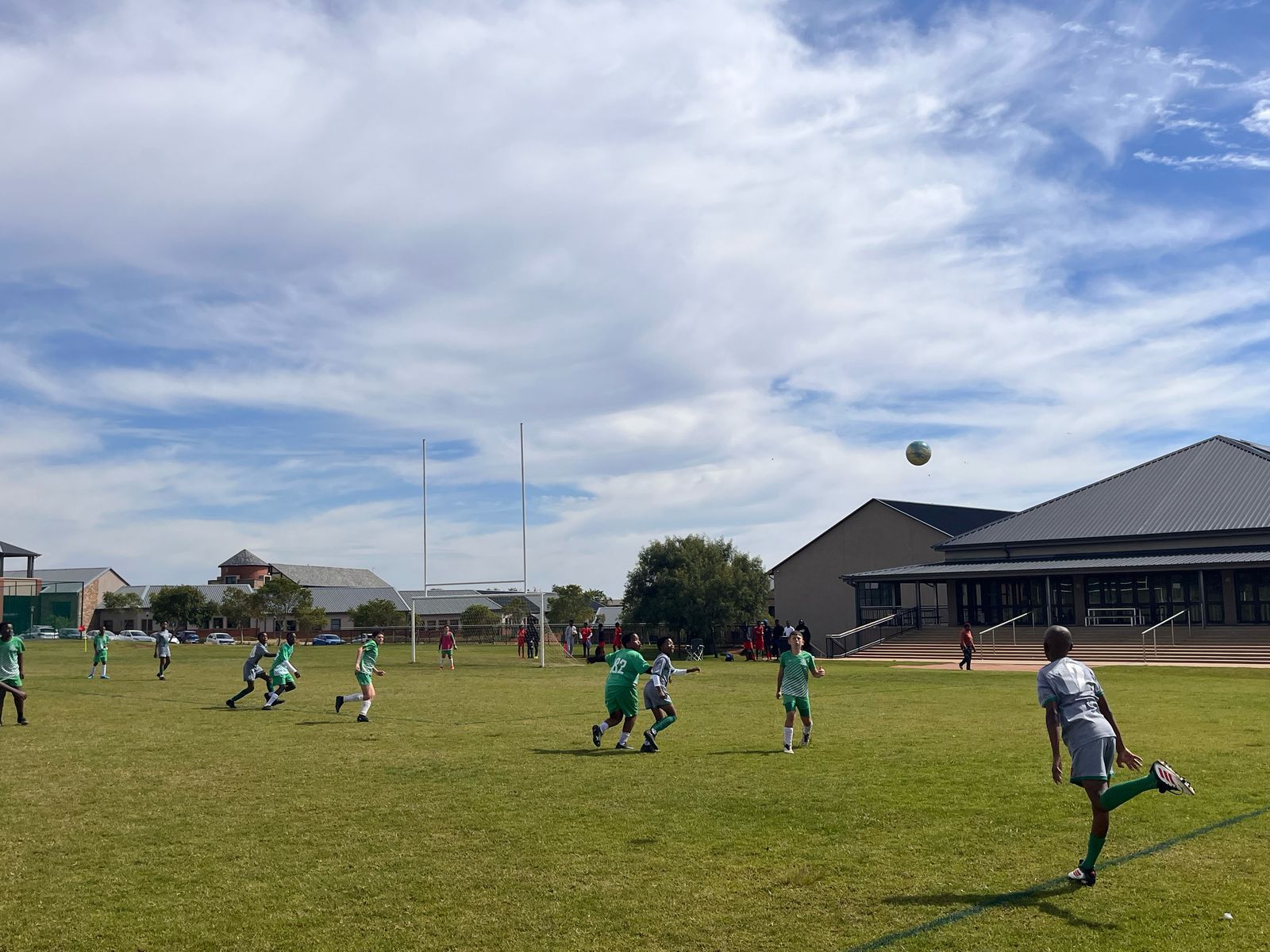 A group of people wearing green and gray uniforms play a game on a grass field under a cloudy sky.
