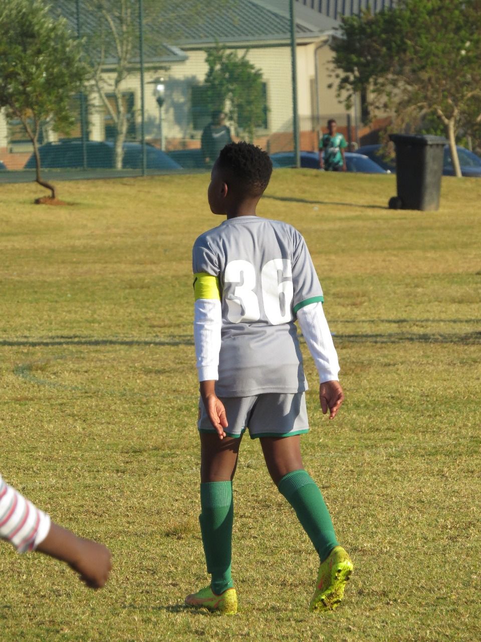 A soccer player in a grey jersey with the number 36 and green socks stands on a grassy field during a game.