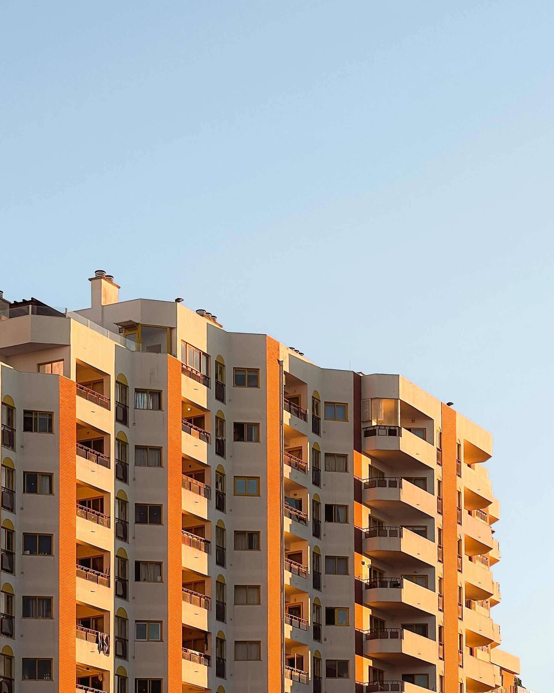 Sunlit apartment building with balconies against a clear blue sky
