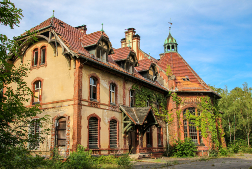 Verlassene historische Villa mit roten Ziegeldächern, Bogenfenstern und üppigem Grün unter blauem Himmel