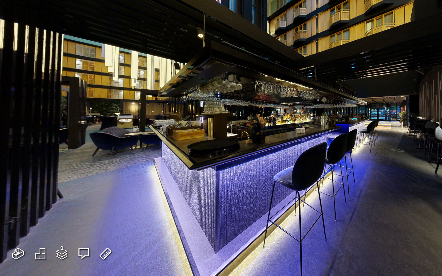 Moderne Bar mit violett beleuchteter Theke und schwarzen Barhockern in einer zeitgenössischen Lounge bei Nacht