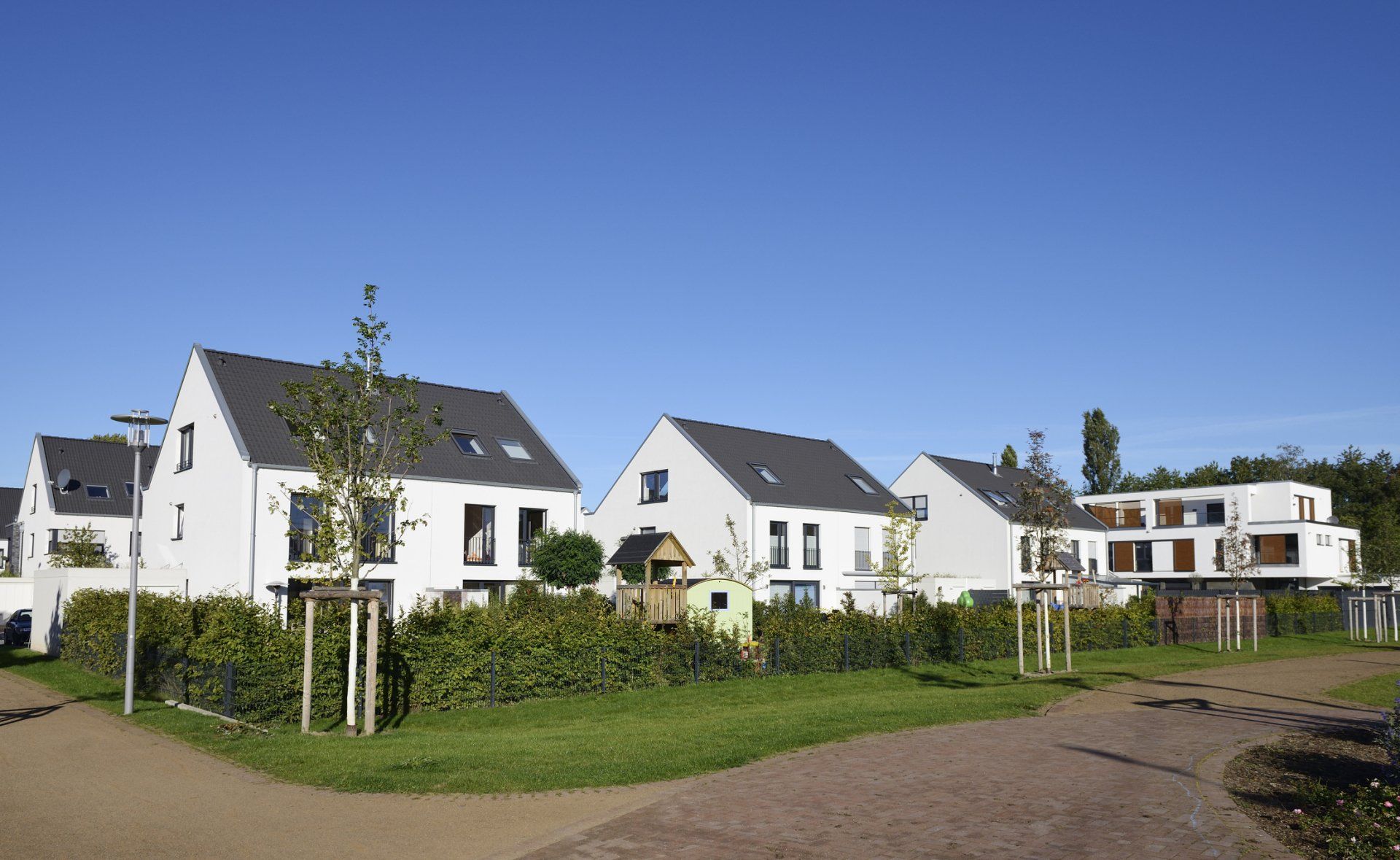 Eine Reihe weißer Häuser mit dunklen Dächern neben einem grünen Rasen unter klarem, blauem Himmel