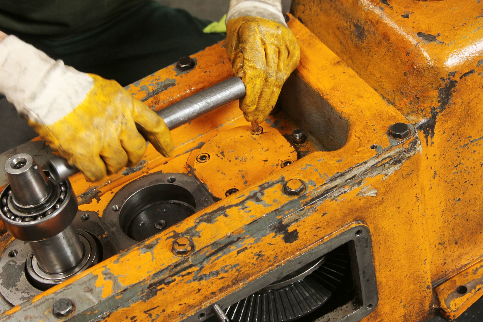 Hands in yellow gloves working on an open, yellow machinery component.