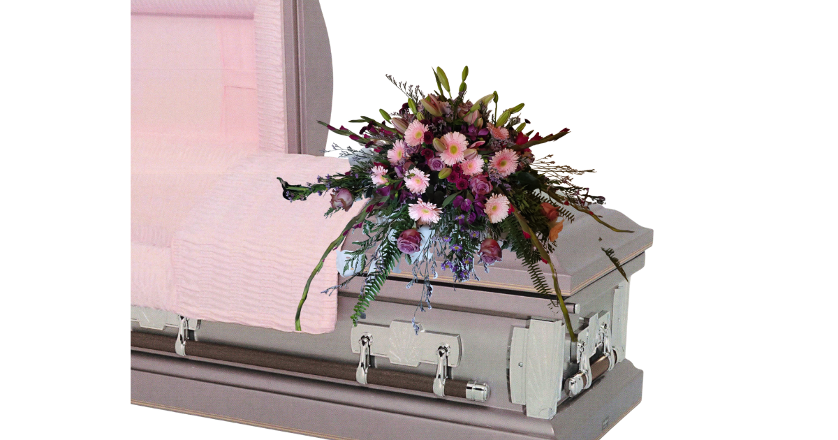 White casket with a pink-and-purple flower arrangement on top, displayed indoors