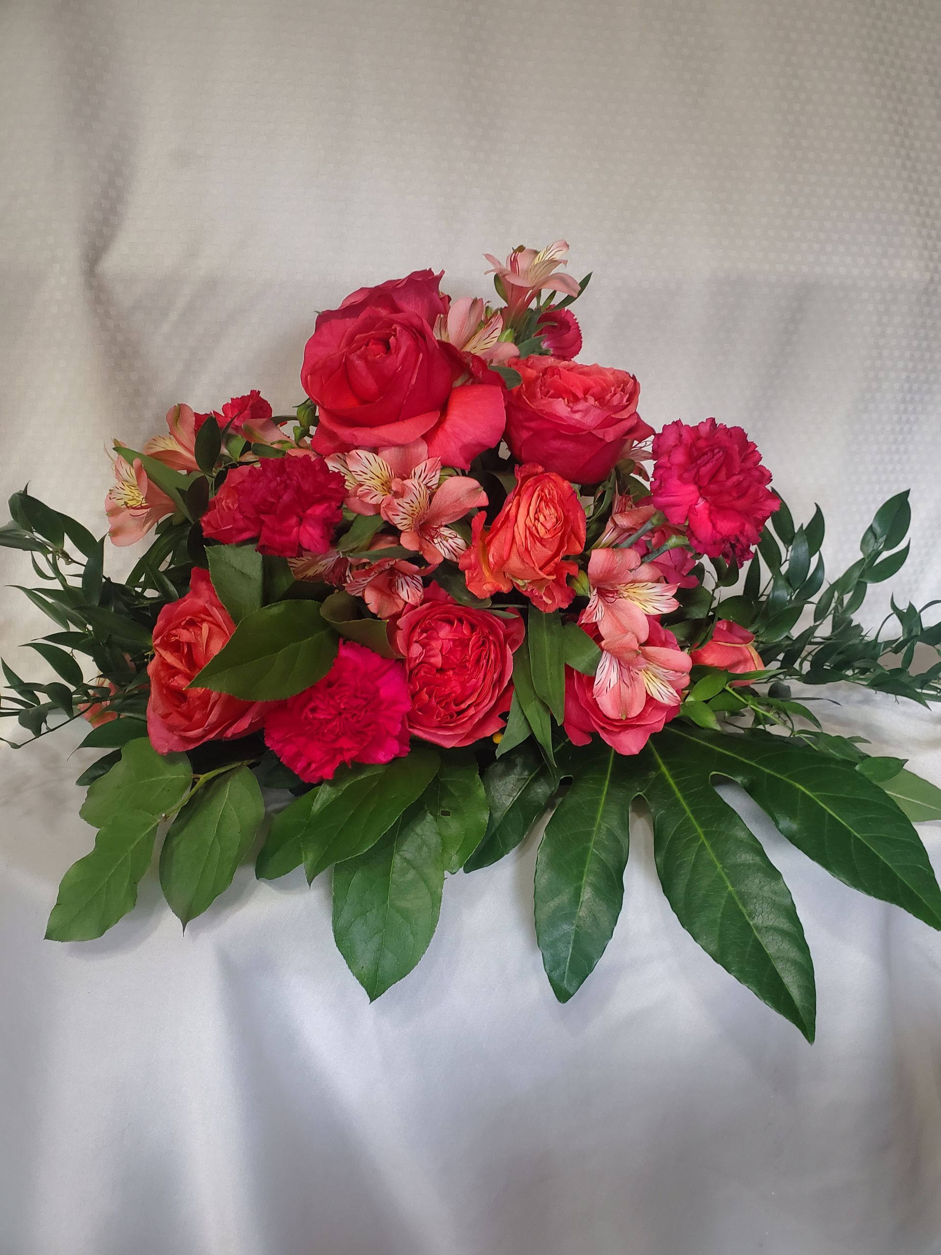 Floral arrangement with red roses, carnations, and greenery on a white surface.