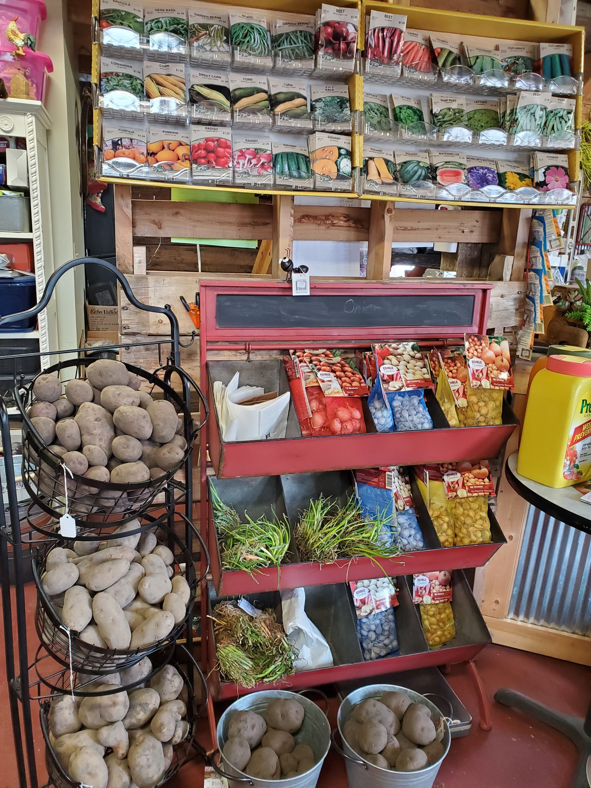 Inside a small store, a display of potato sacks, seed packets, and other produce.