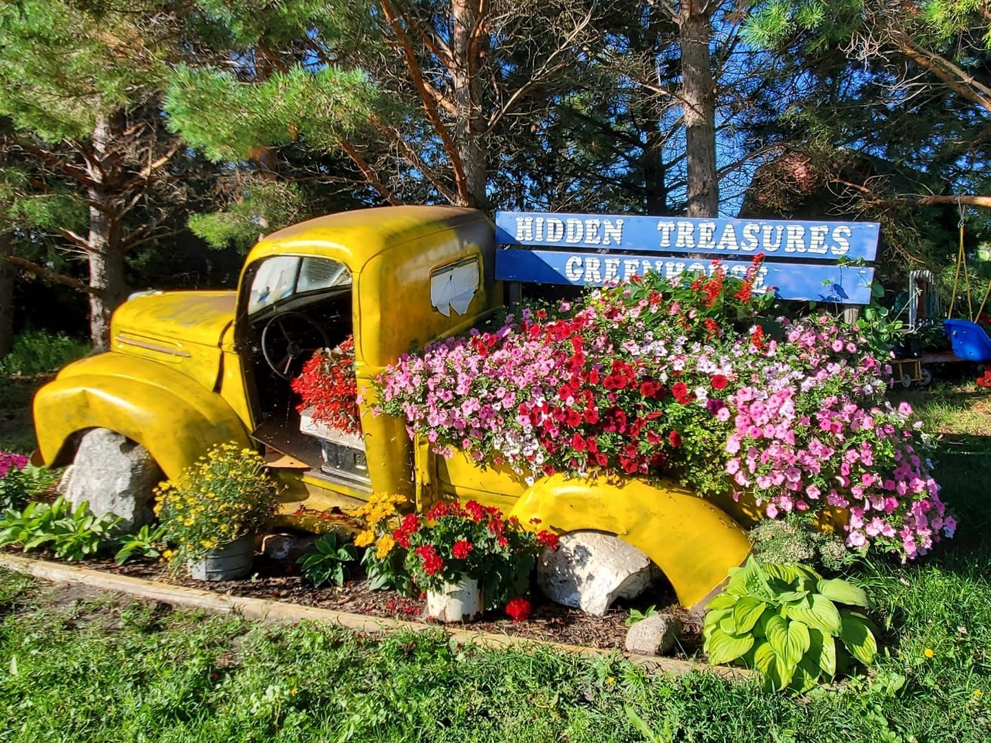 Yellow truck bed overflowing with flowers, in front of a sign that reads