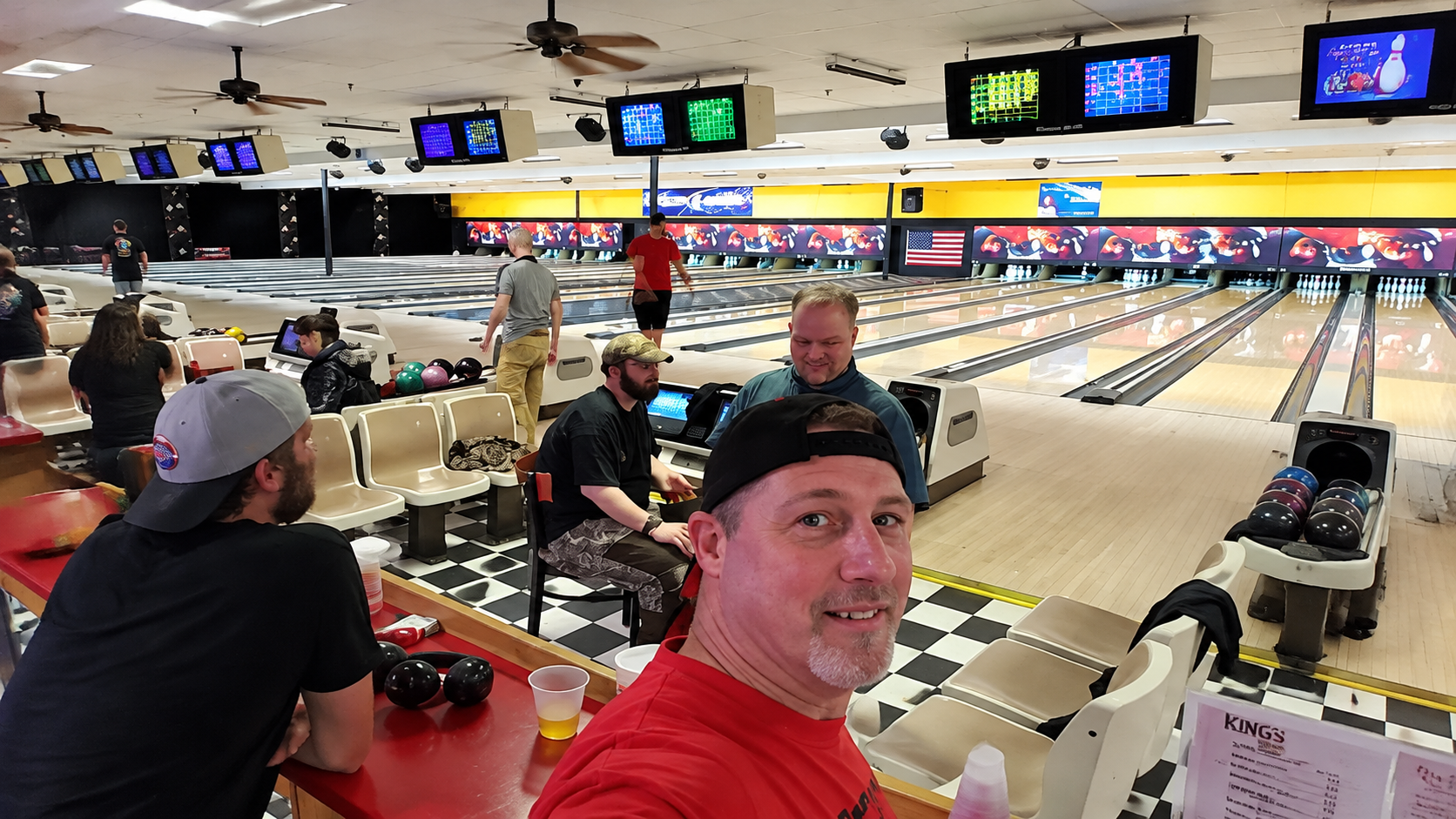 People seated in a bowling alley lounge, one person taking a selfie in the foreground.