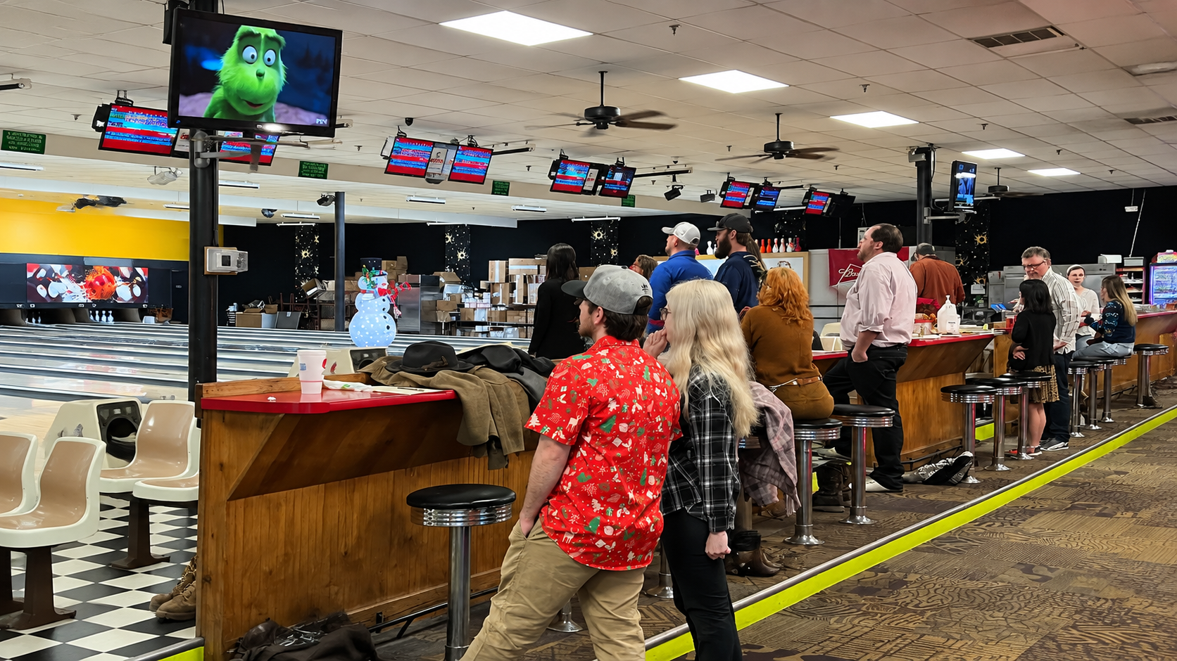 Crowded bowling alley with people waiting near lanes and seating area under bright ceiling lights
