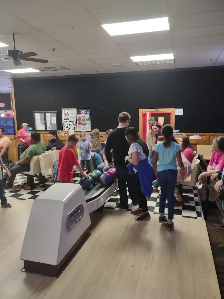 Crowded bowling alley with people waiting near lanes and seating area under bright ceiling lights