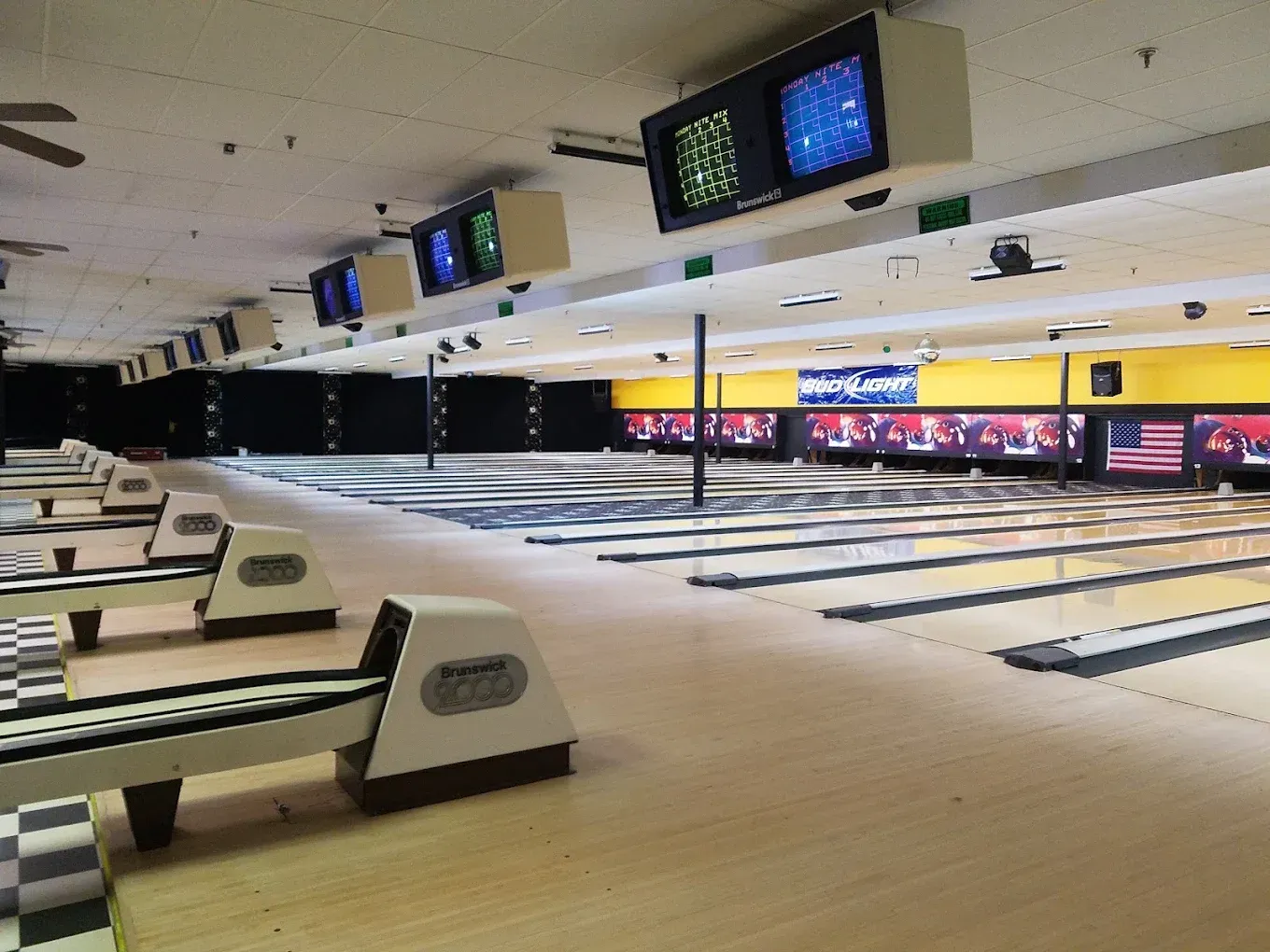 Bowling alley with empty lanes, ball returns, and overhead scoreboards under bright lights