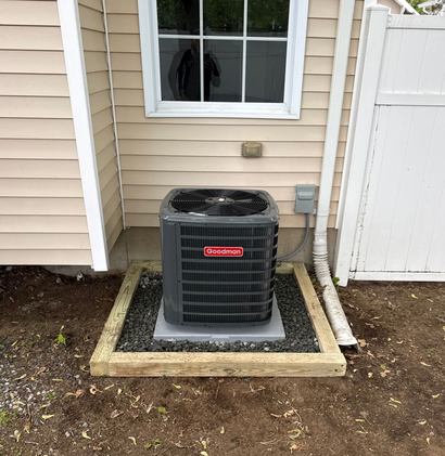 Outdoor air conditioner unit beside a house, surrounded by a small gravel and concrete border.