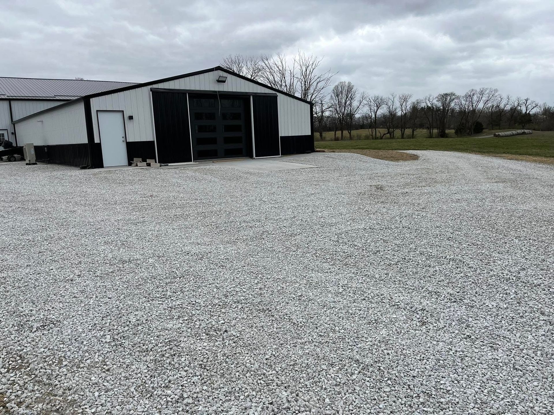 White and black barn on gravel, cloudy sky.